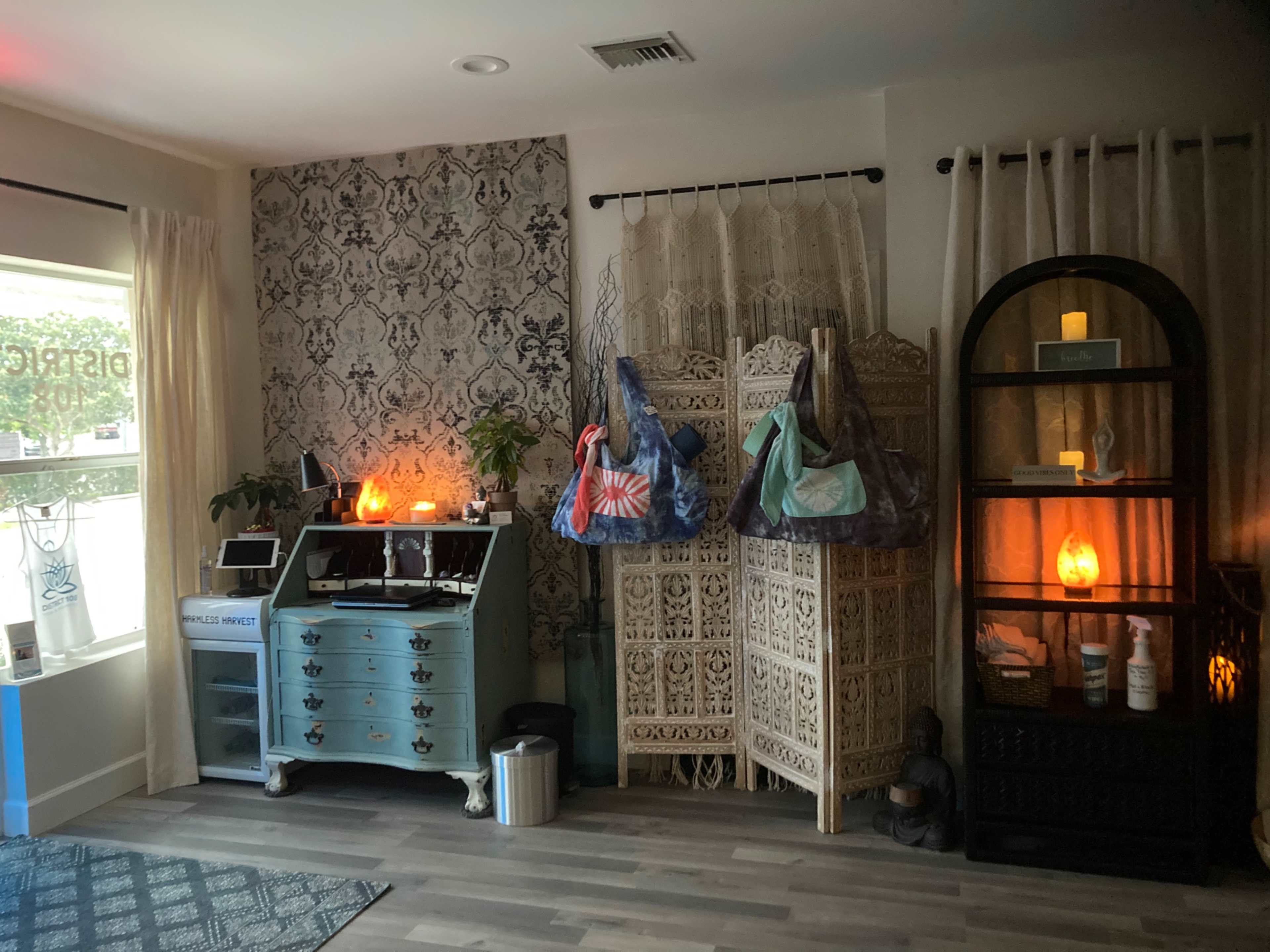 The room features a combination of decorative elements, including a blue dresser, several hanging bags, a wooden screen, and a black shelving unit with candles and a salt lamp.