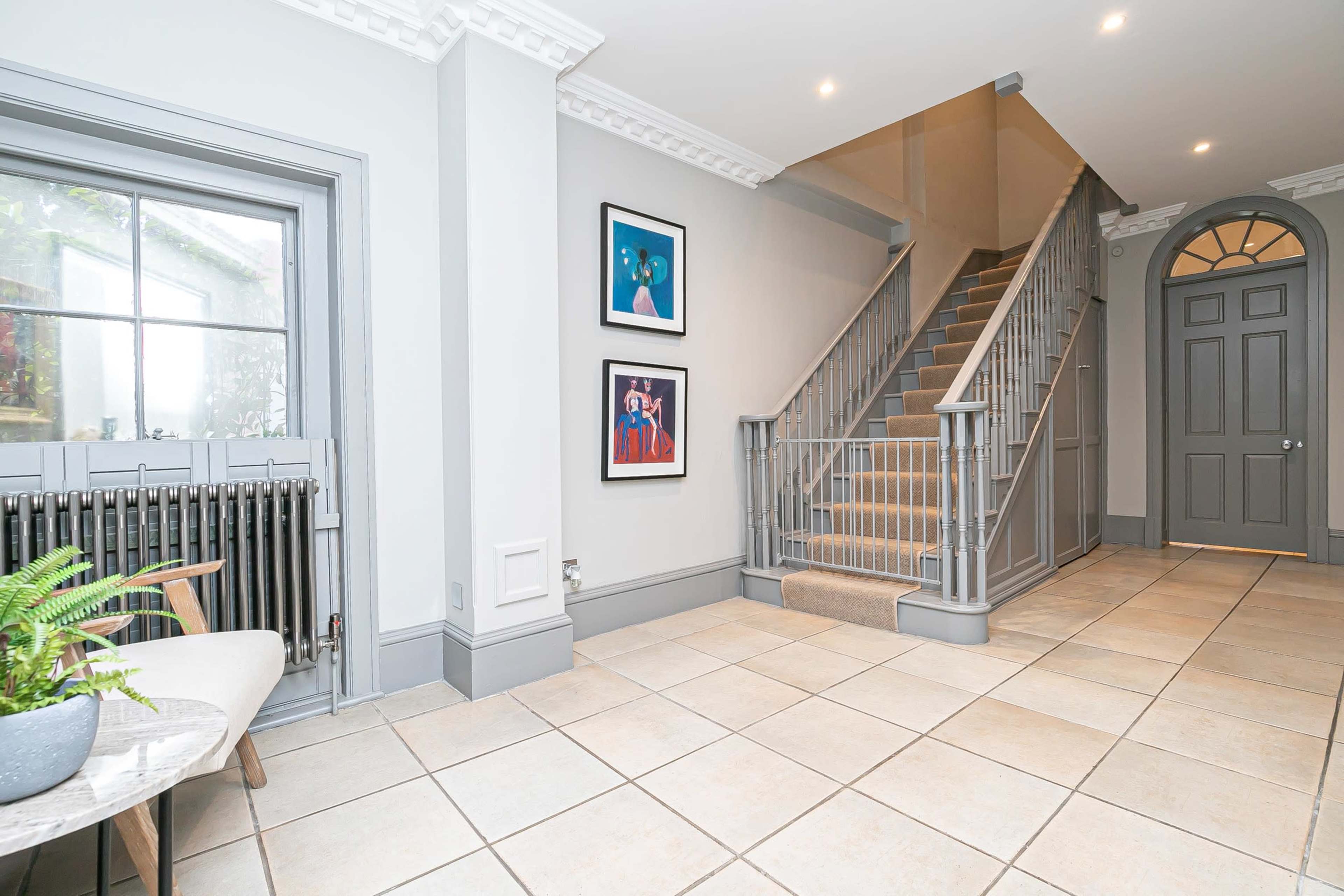 A spacious hallway with a staircase, framed artwork on the walls, and tiled flooring.