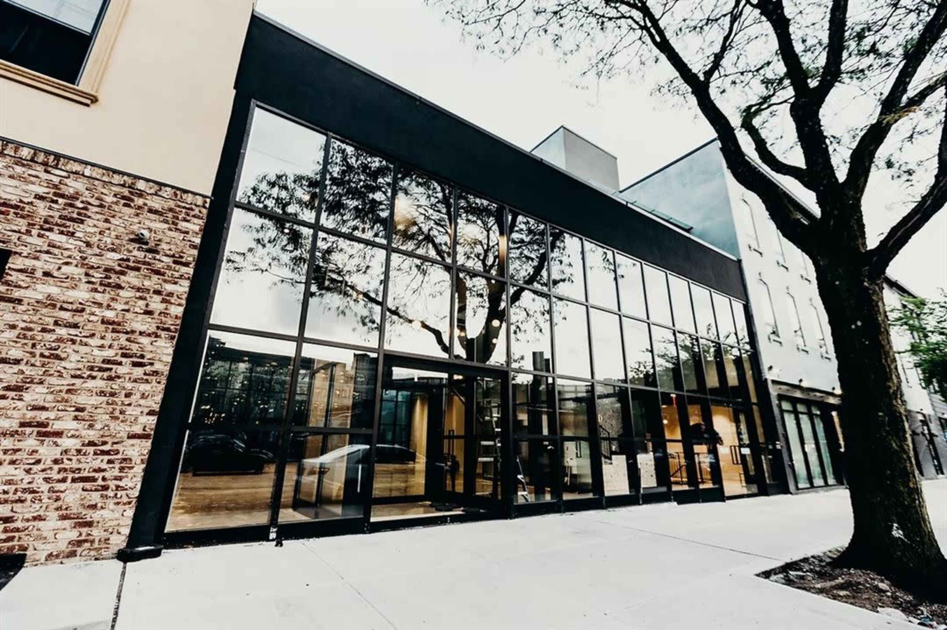 A modern building with large glass windows and a brick facade, surrounded by trees on a sidewalk.