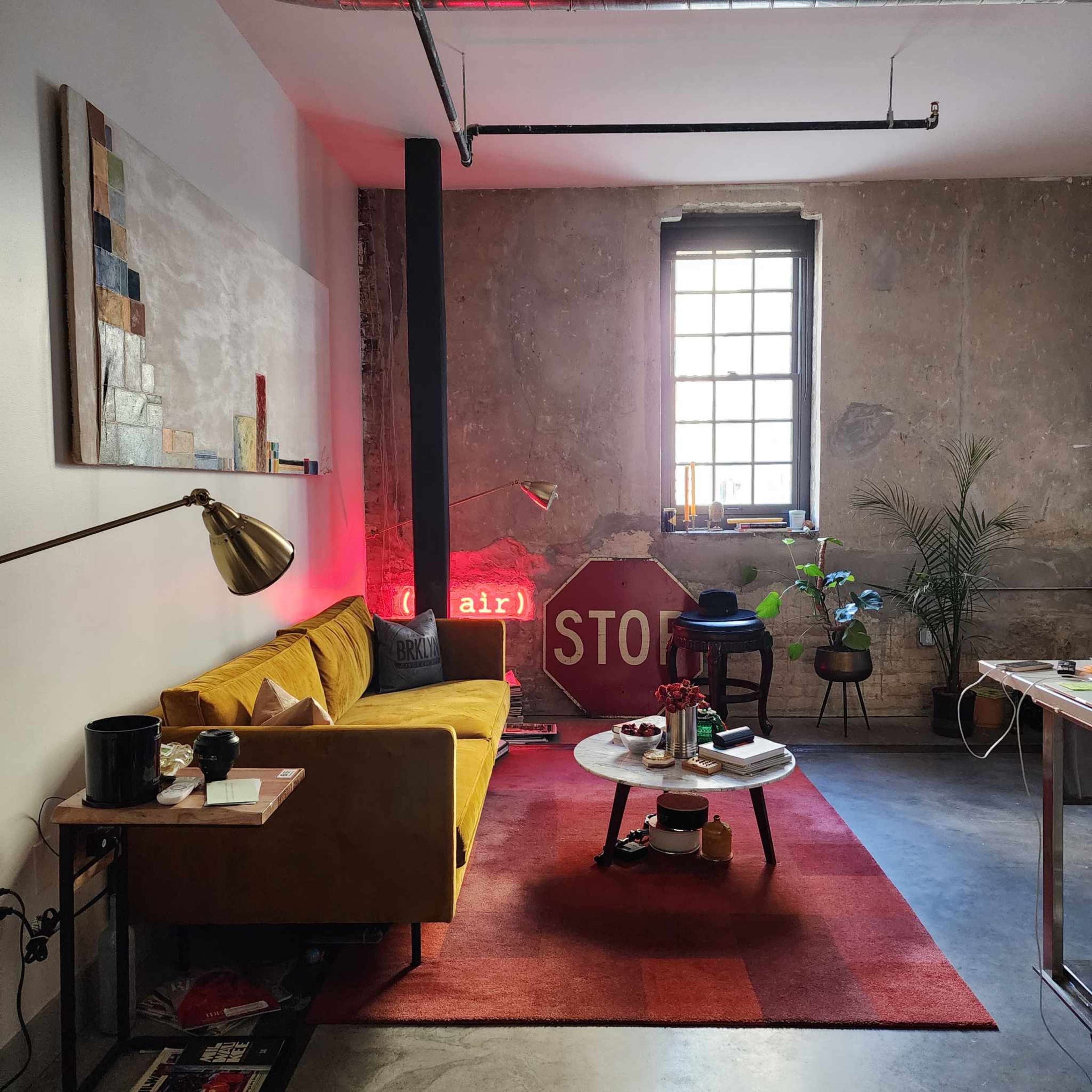 The scene features a cozy living area with a yellow sofa, a round coffee table, and a neon sign illuminated against a textured wall, alongside a window and indoor plants.