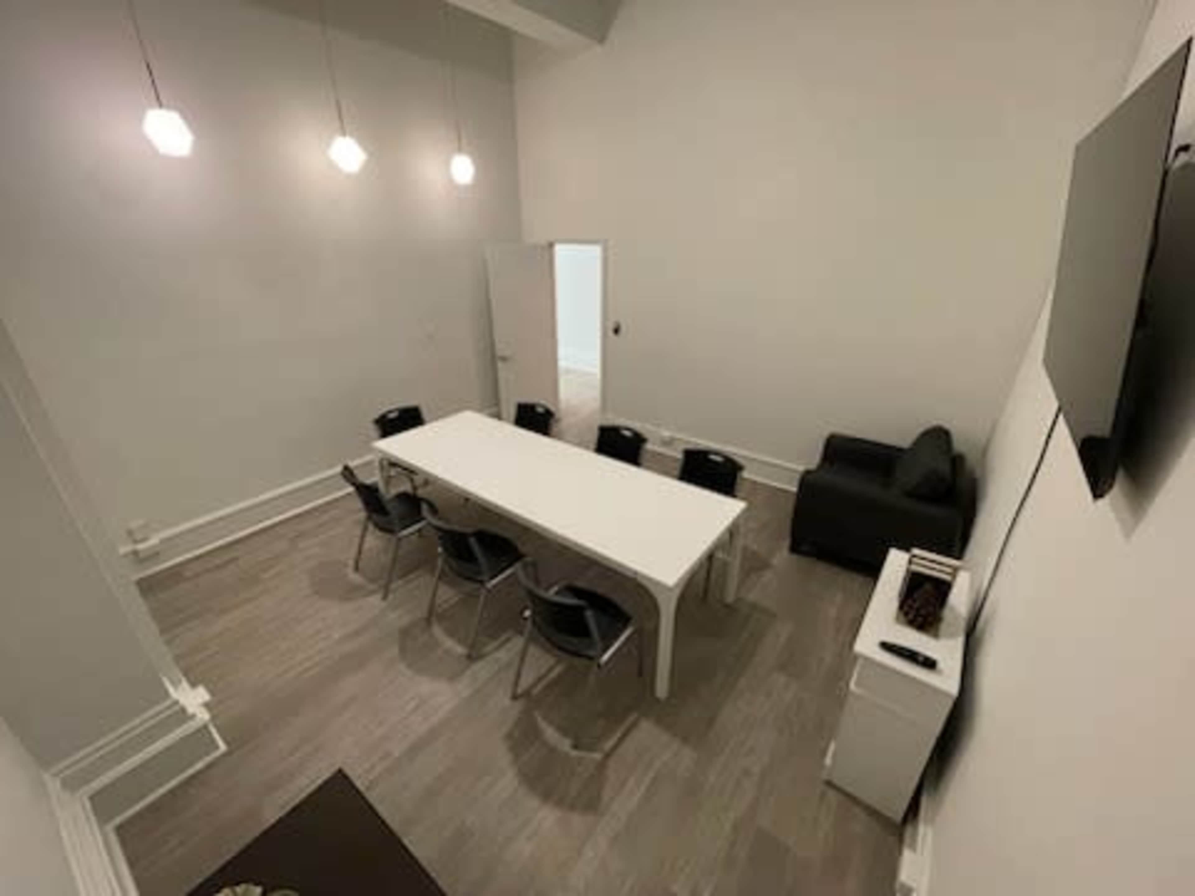 A modern meeting room with a white table, black chairs, a sofa, and a wall-mounted television.