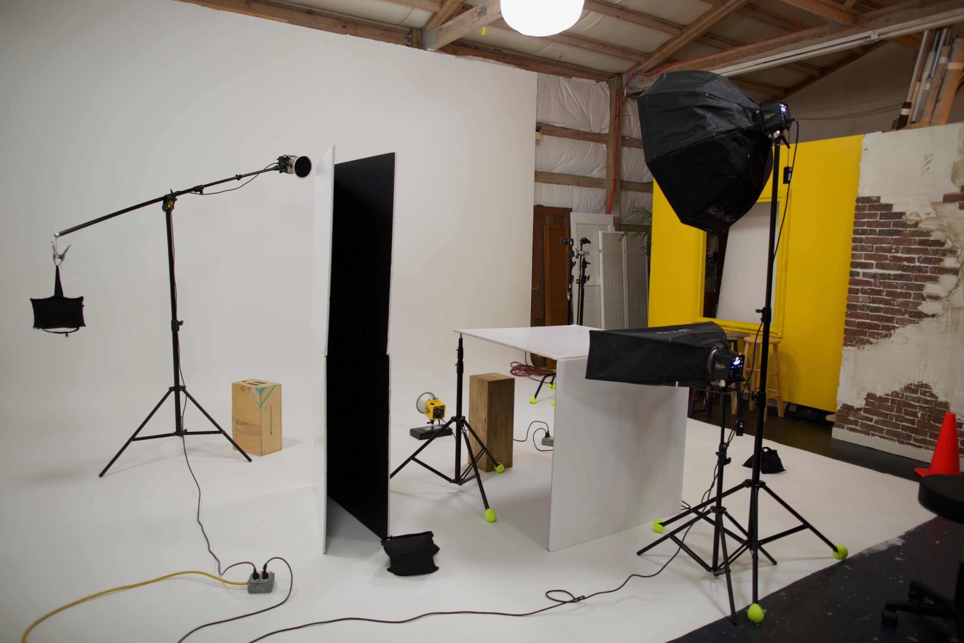 A photography studio setup featuring a white backdrop, a table, several light stands, and various equipment positioned on a white floor.
