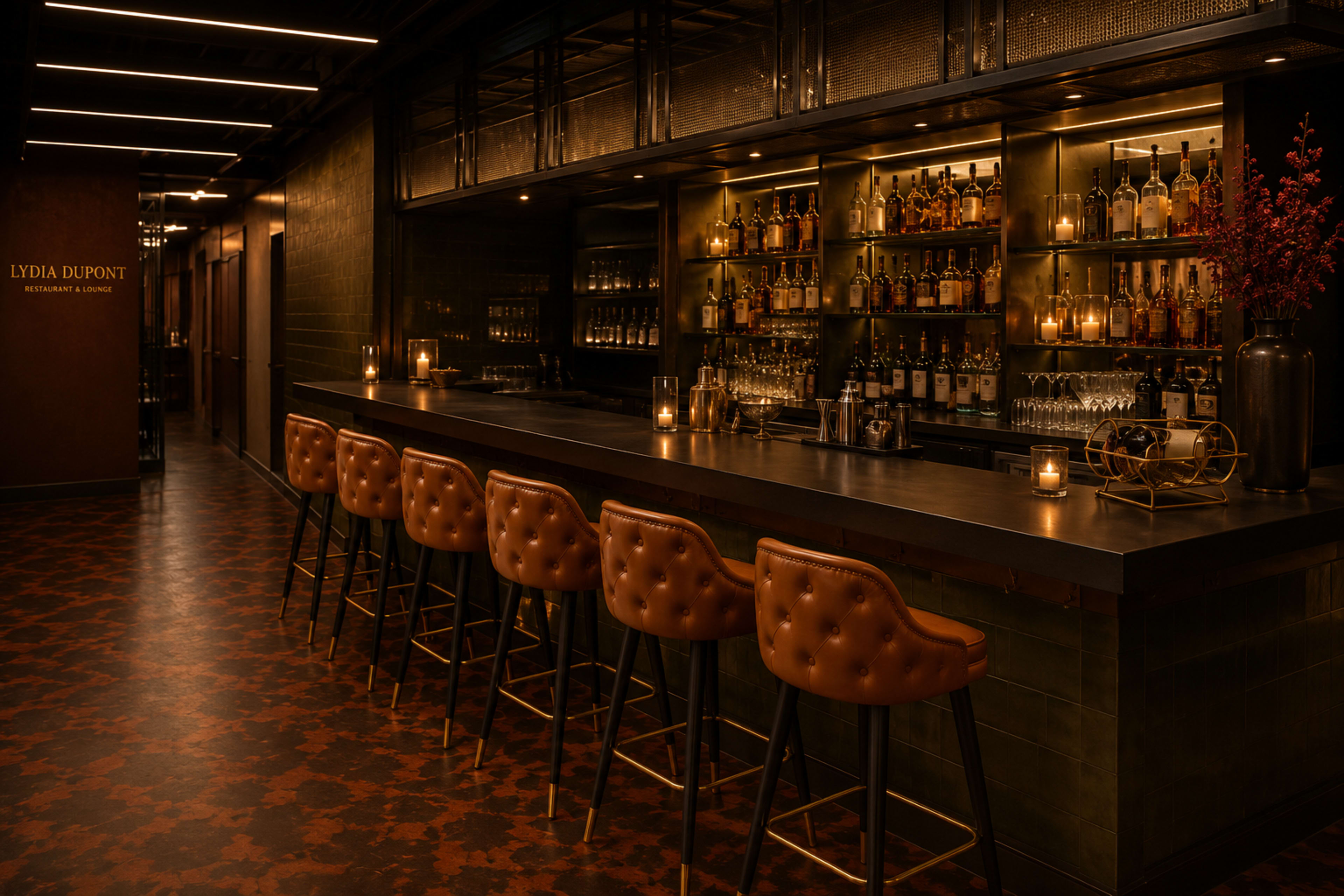 The image shows a dimly lit bar area with a long countertop, upholstered stools, and shelves lined with various bottles of alcohol, accompanied by candlelight and modern decor.