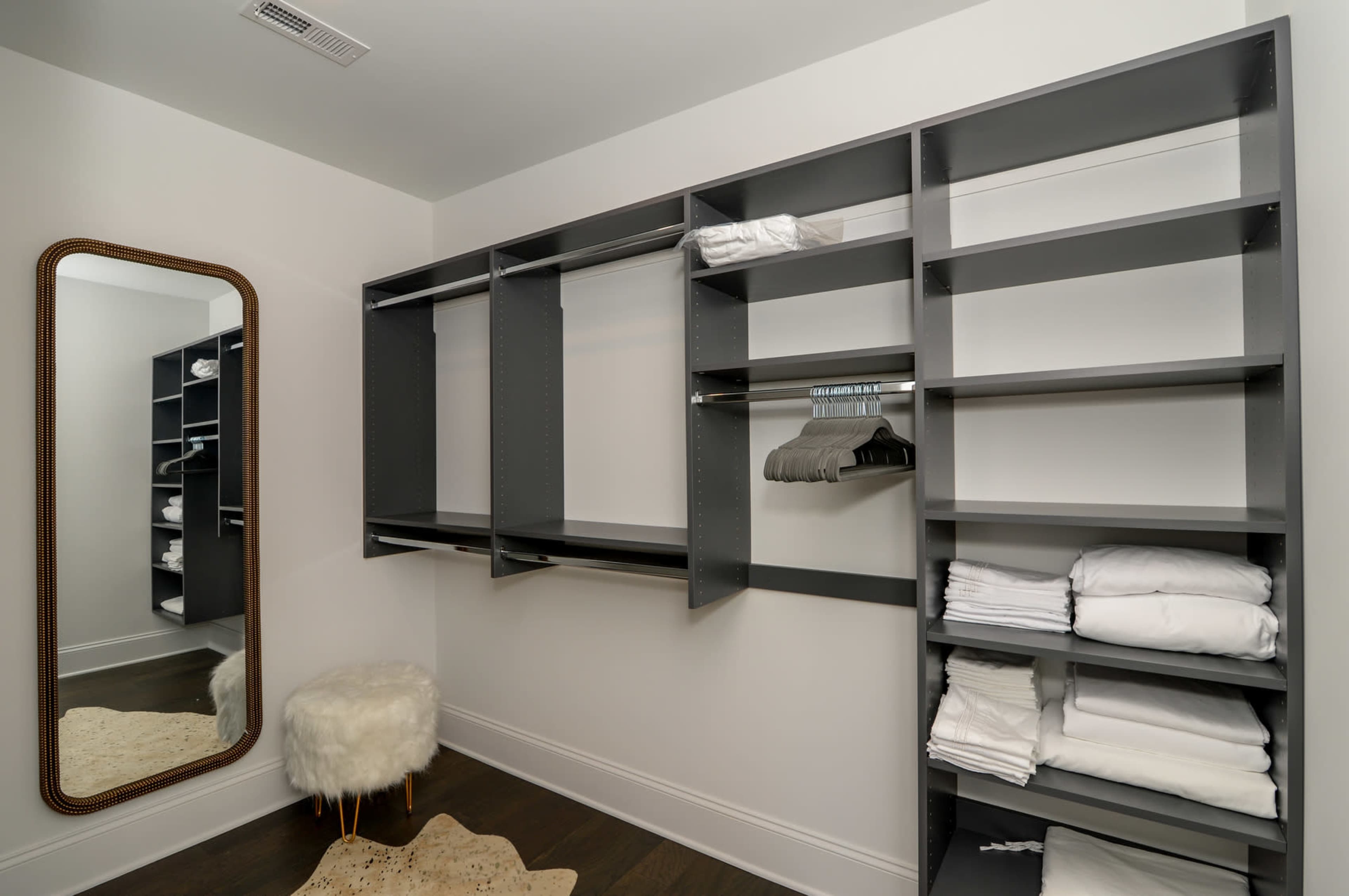 A minimalist closet features gray shelving, hanging space, neatly folded towels, and a full-length mirror reflecting the room's layout.