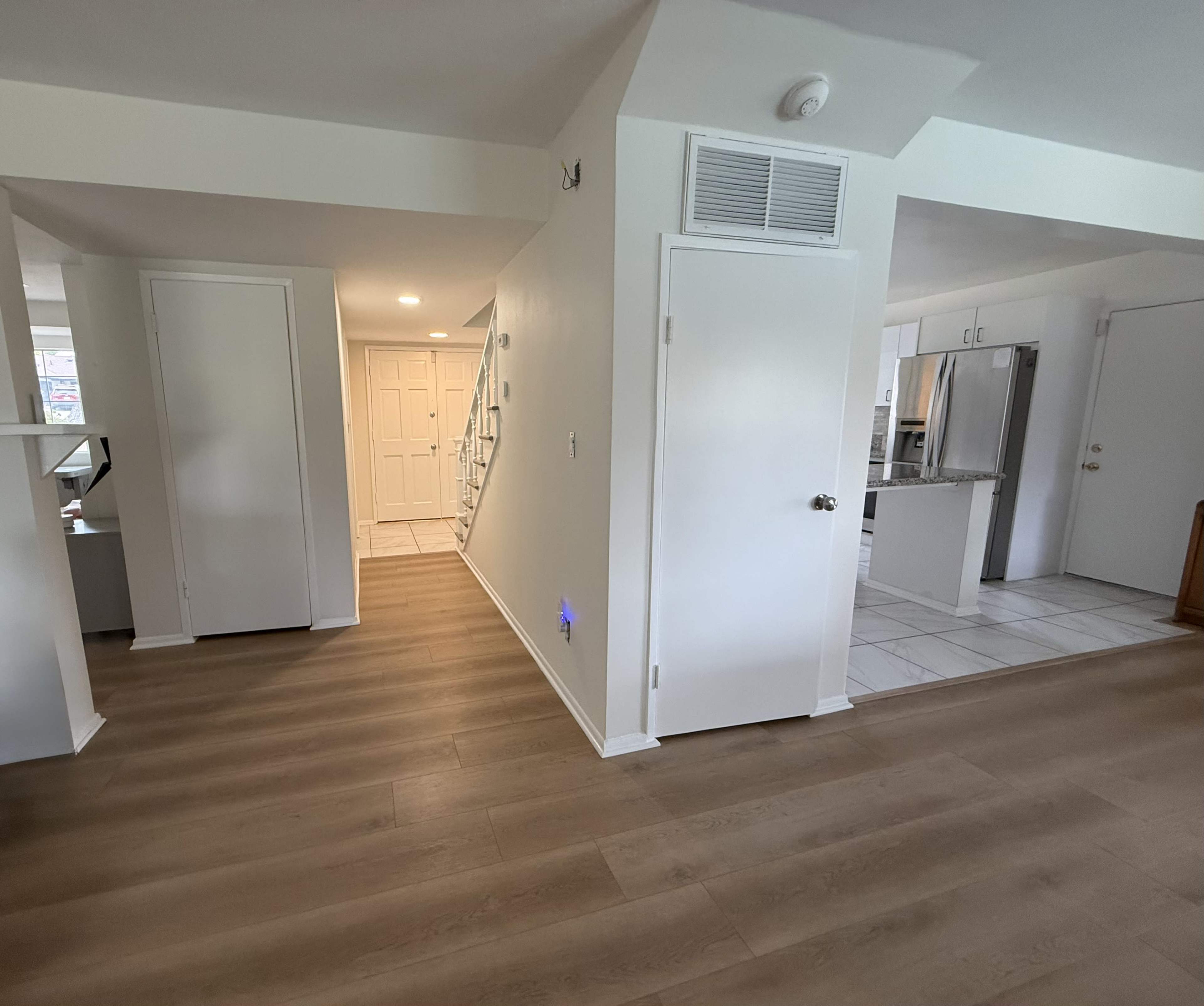 The image shows a spacious hallway with light-colored hardwood floors, leading to a staircase on the left and an open kitchen area on the right.