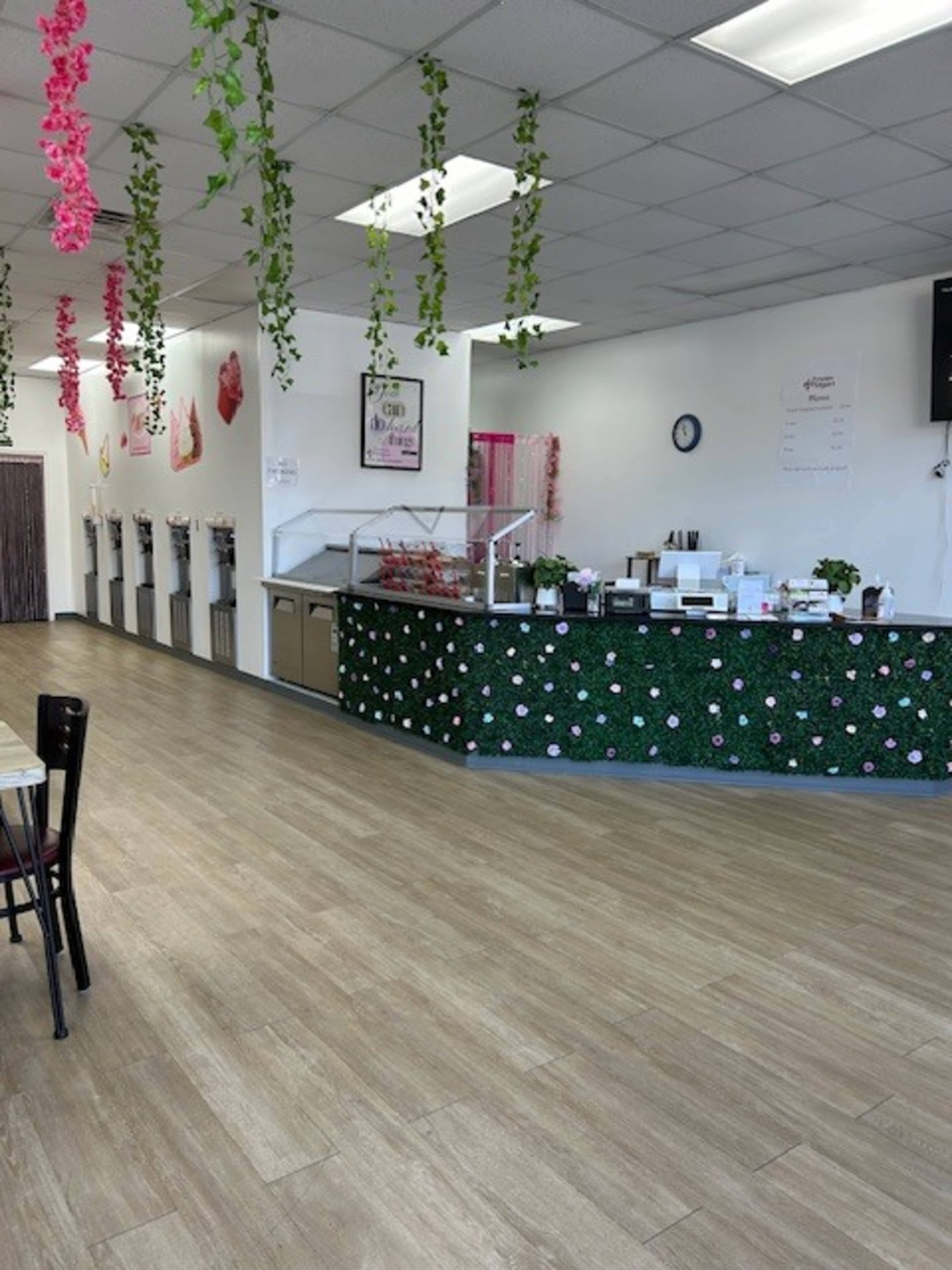 The image shows the interior of a cafe with a service counter adorned with decorative greenery and flowers, along with a spacious seating area.