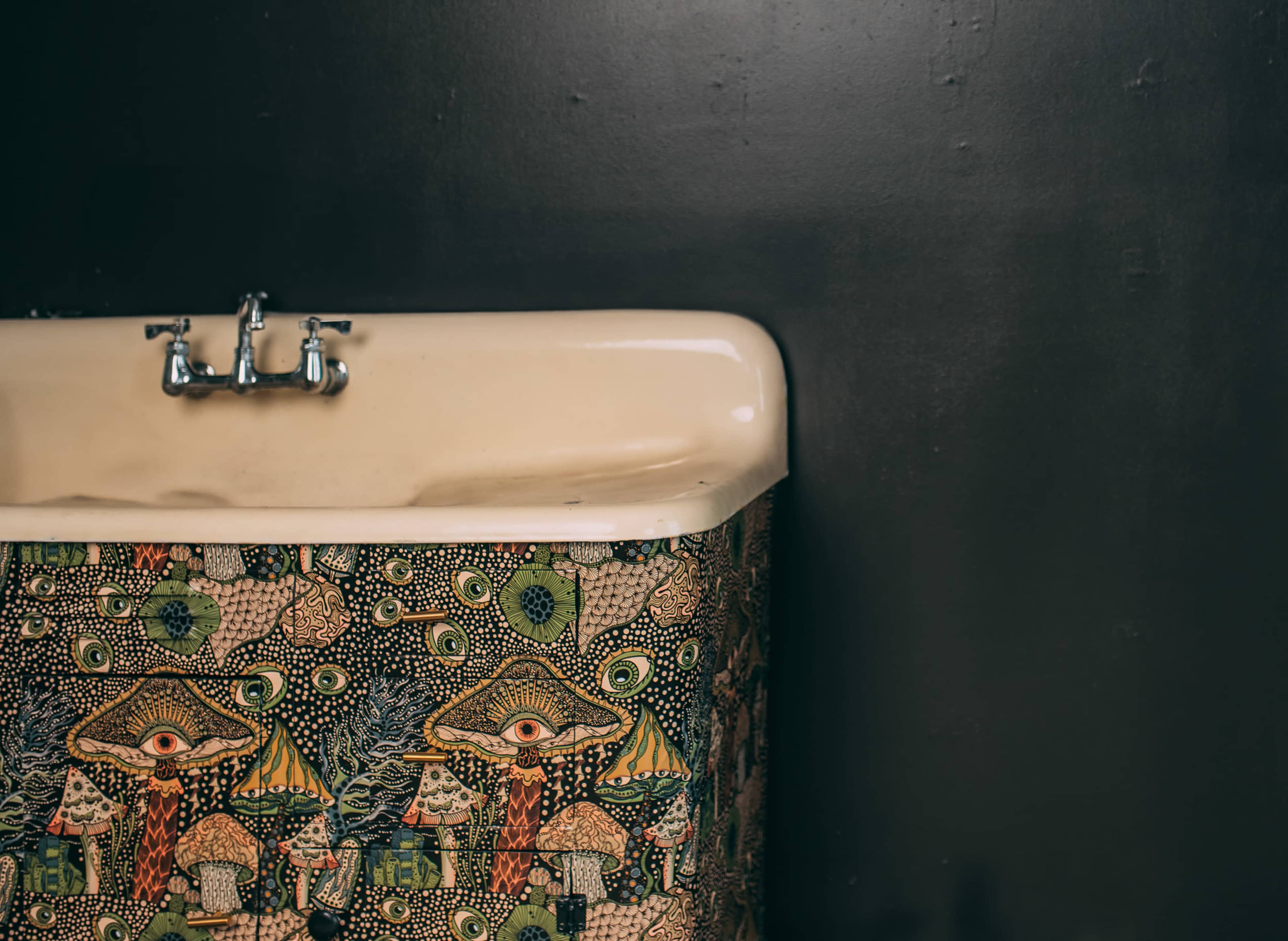 A sink with a patterned basin featuring colorful mushroom and eye designs is mounted against a dark wall.