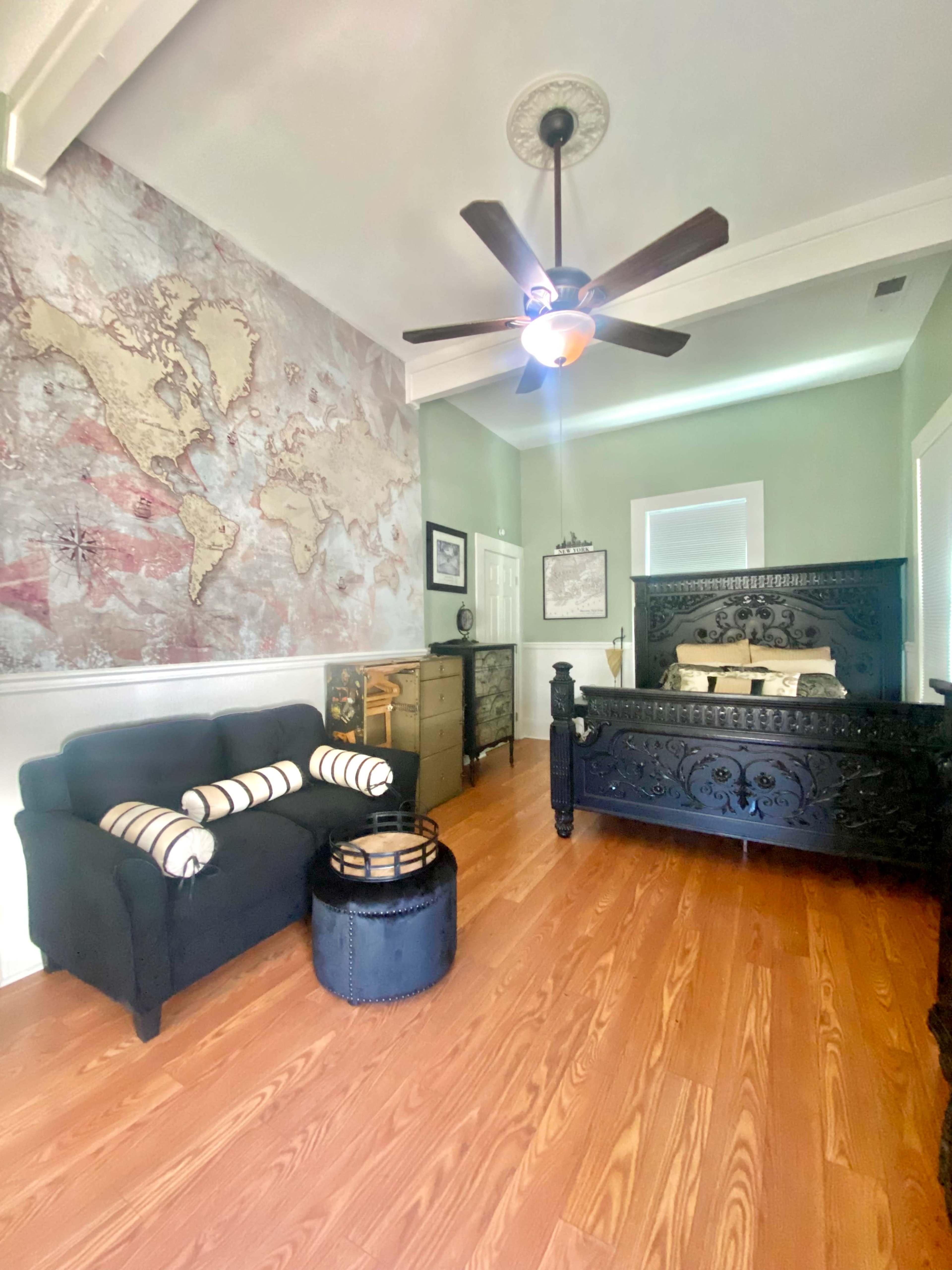 A room featuring a large world map mural, an ornate black bed, a dark coffee table, and a small seating area with striped cushions.