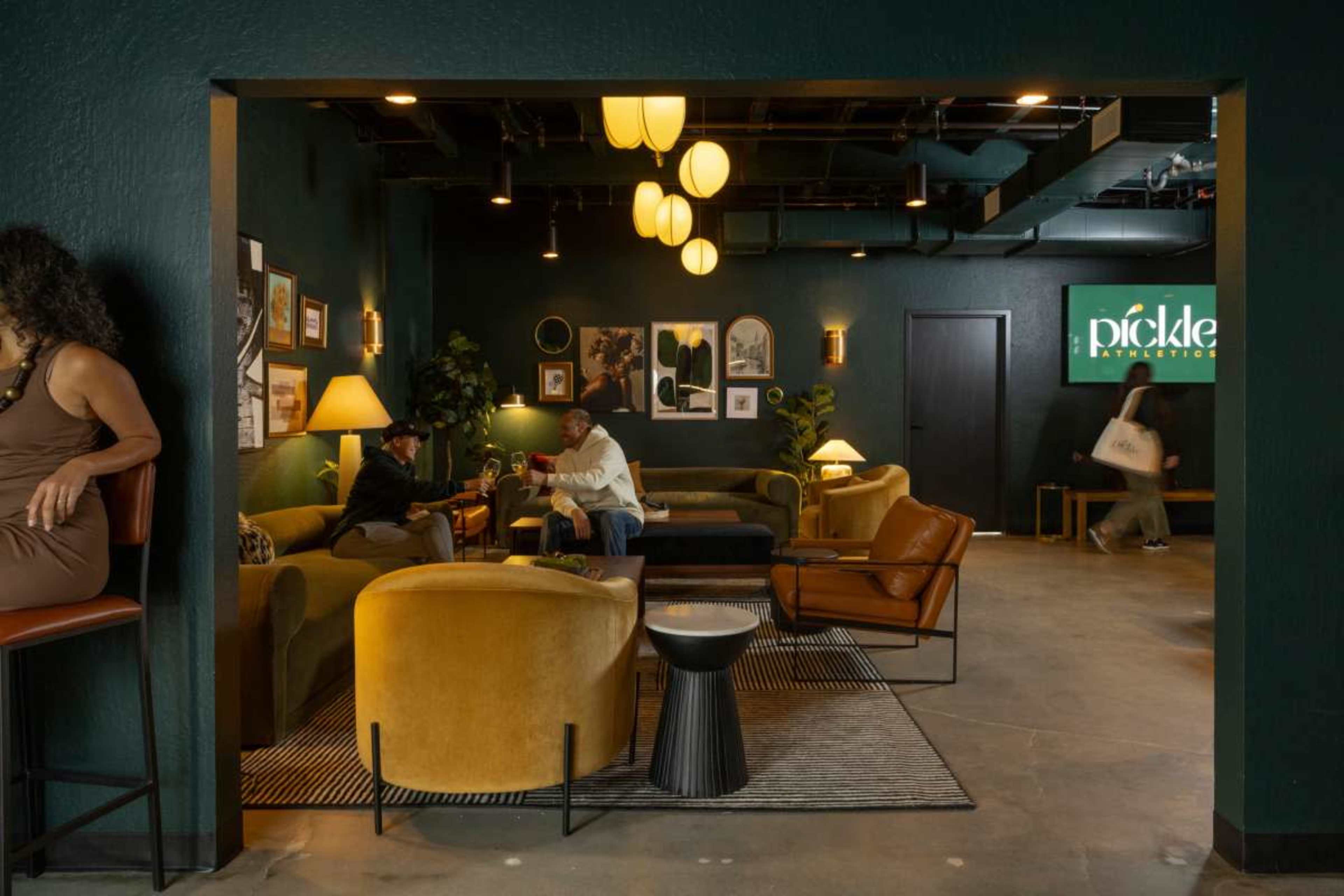The image shows a modern lounge area with green walls, various seating options, and decorative artwork.