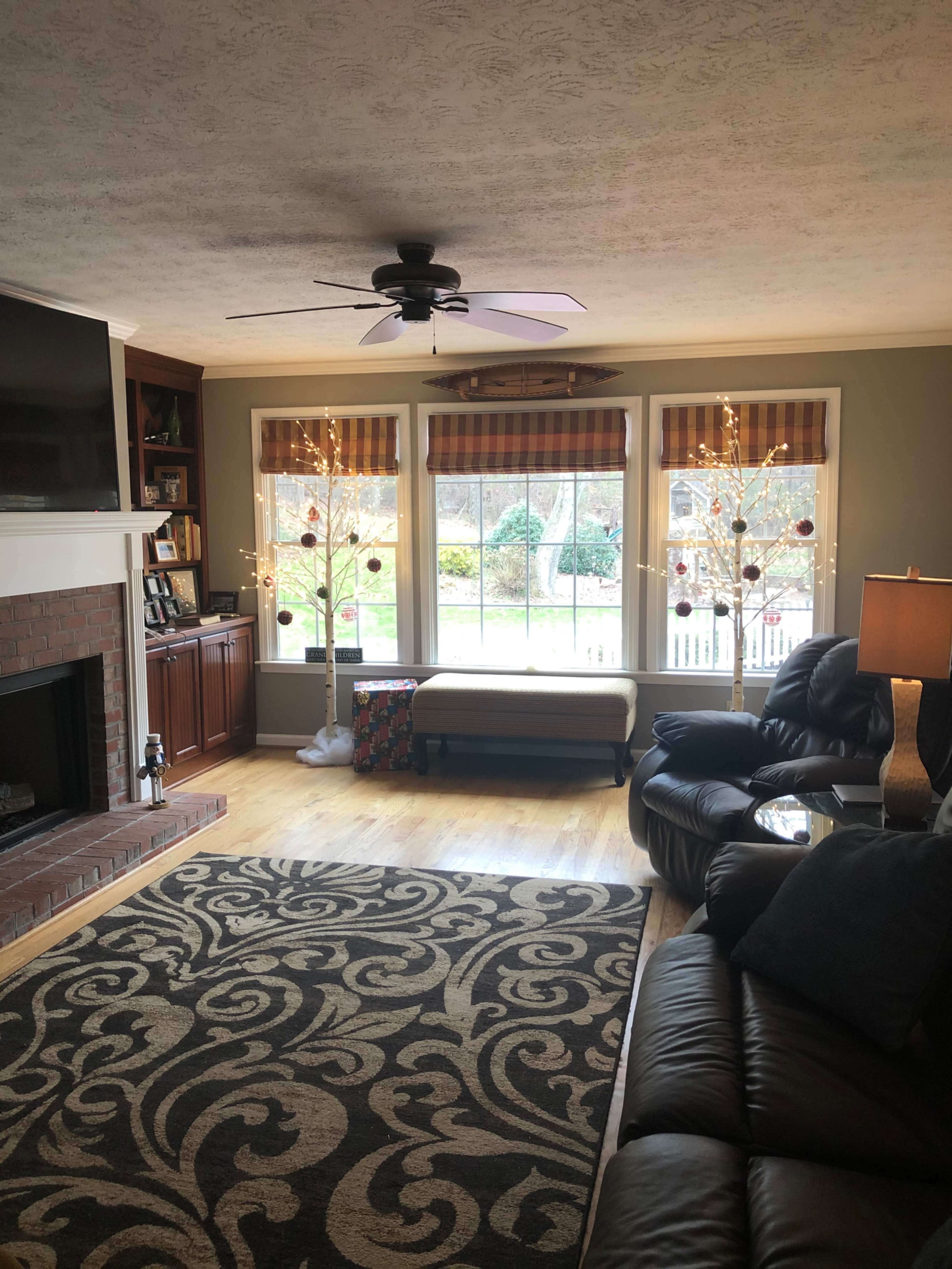 The living room features a large window with two decorated trees, a fireplace, and a leather seating area, all illuminated by natural light.
