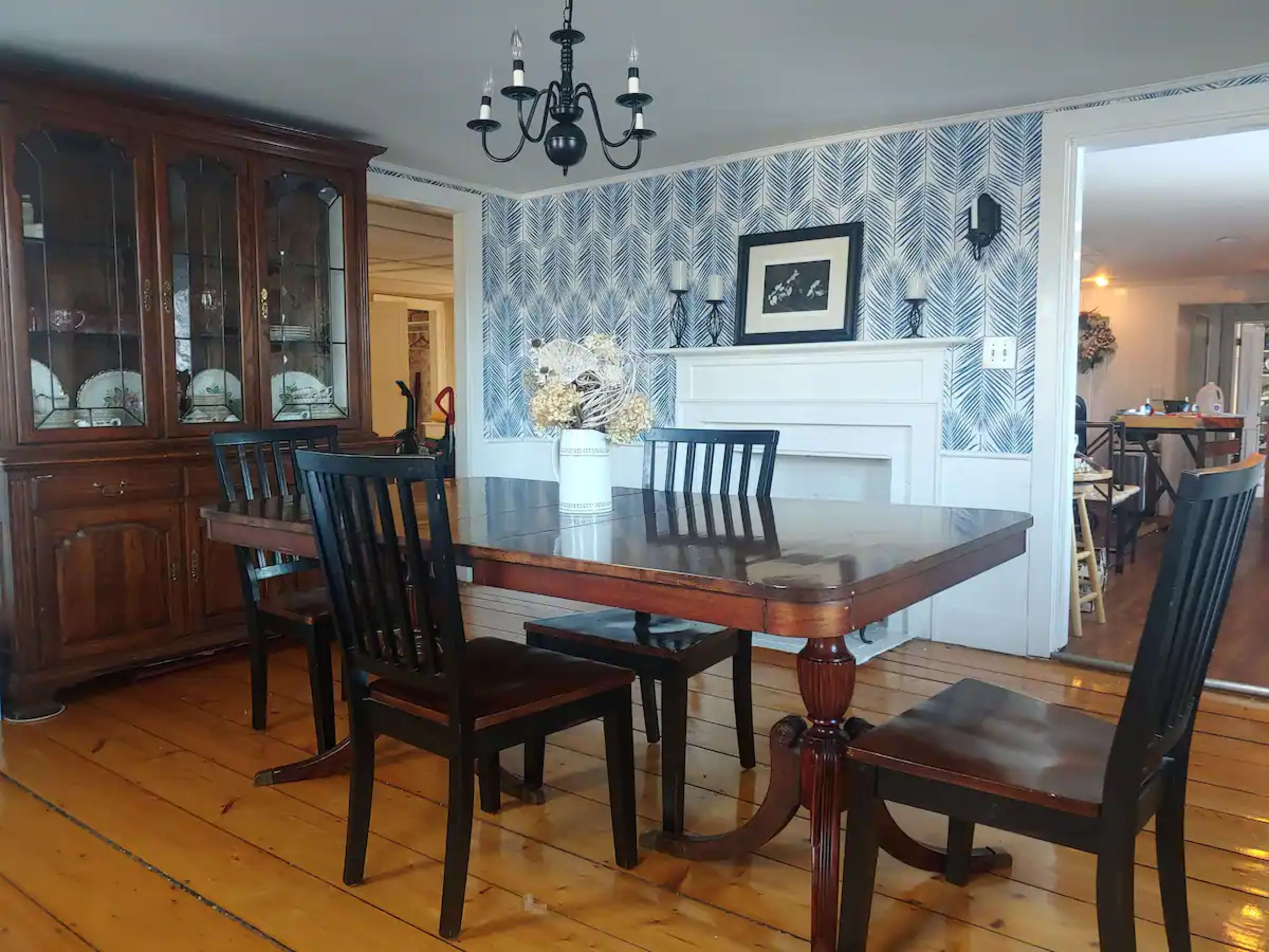 A dining room with a wooden table surrounded by black chairs, a chandelier above, and a china cabinet against the wall.