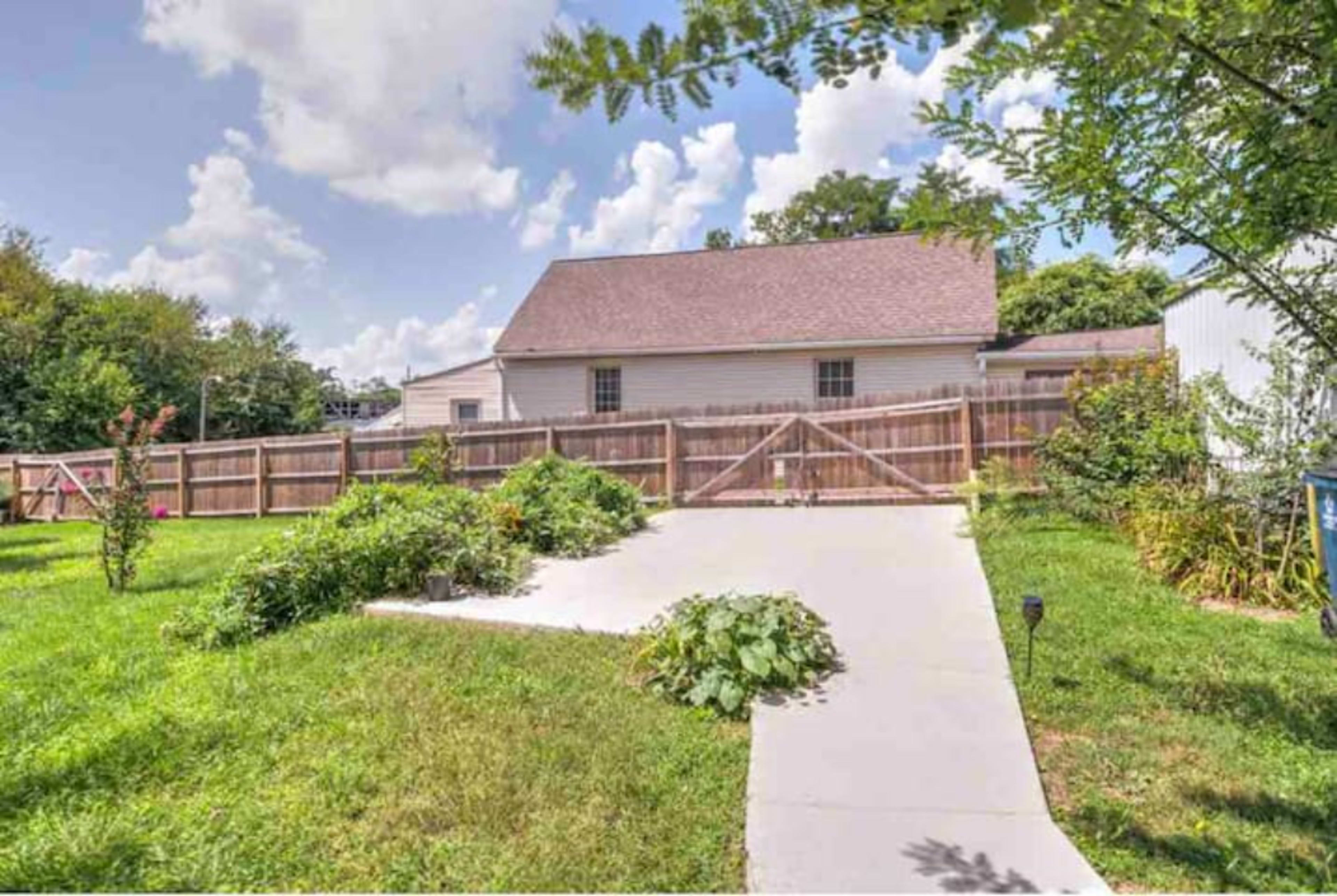 A residential backyard features a concrete pathway leading to a wooden gate, surrounded by grassy areas and shrubs.