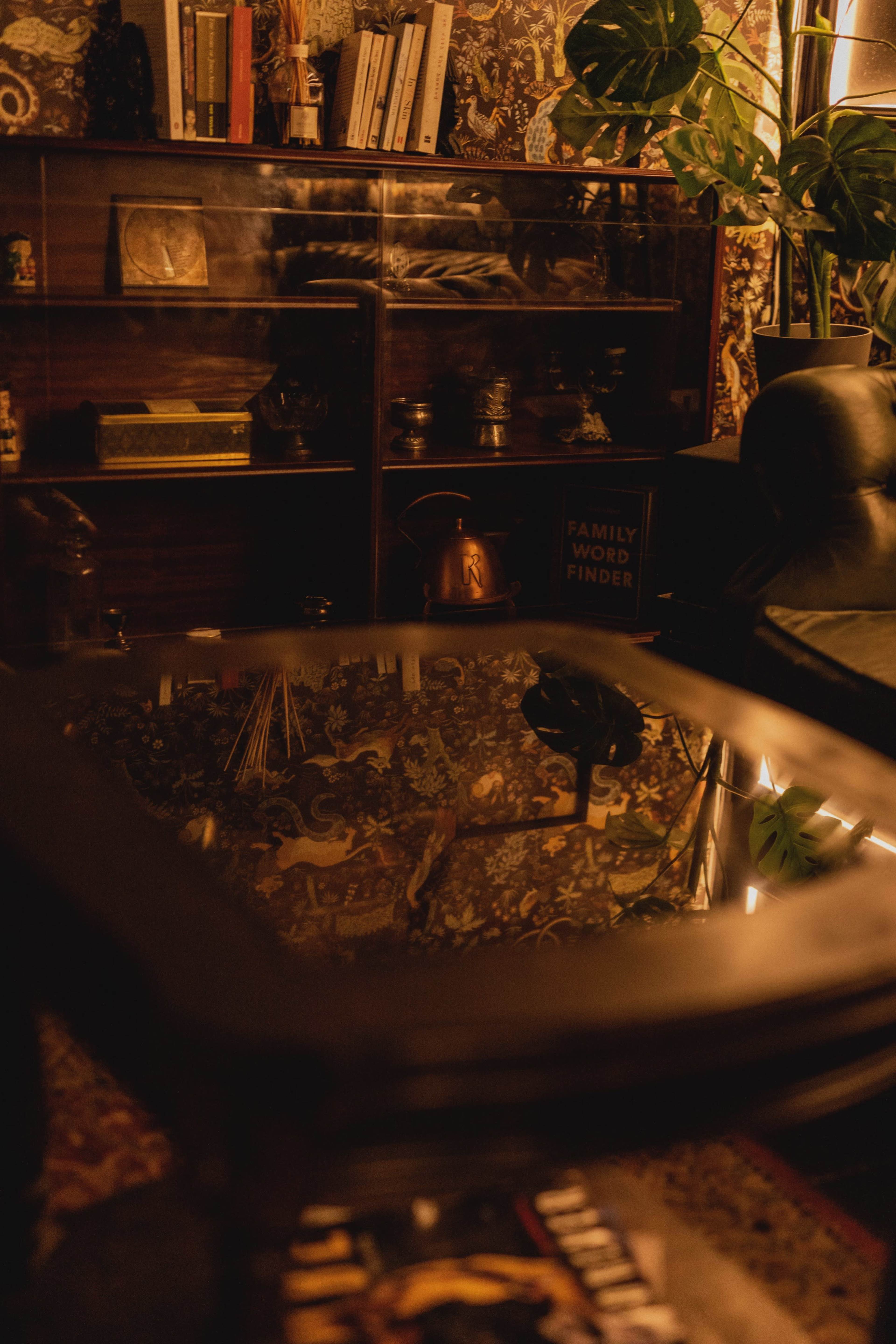 A wooden table reflecting the shelves filled with books and decorative items in a dimly lit room.