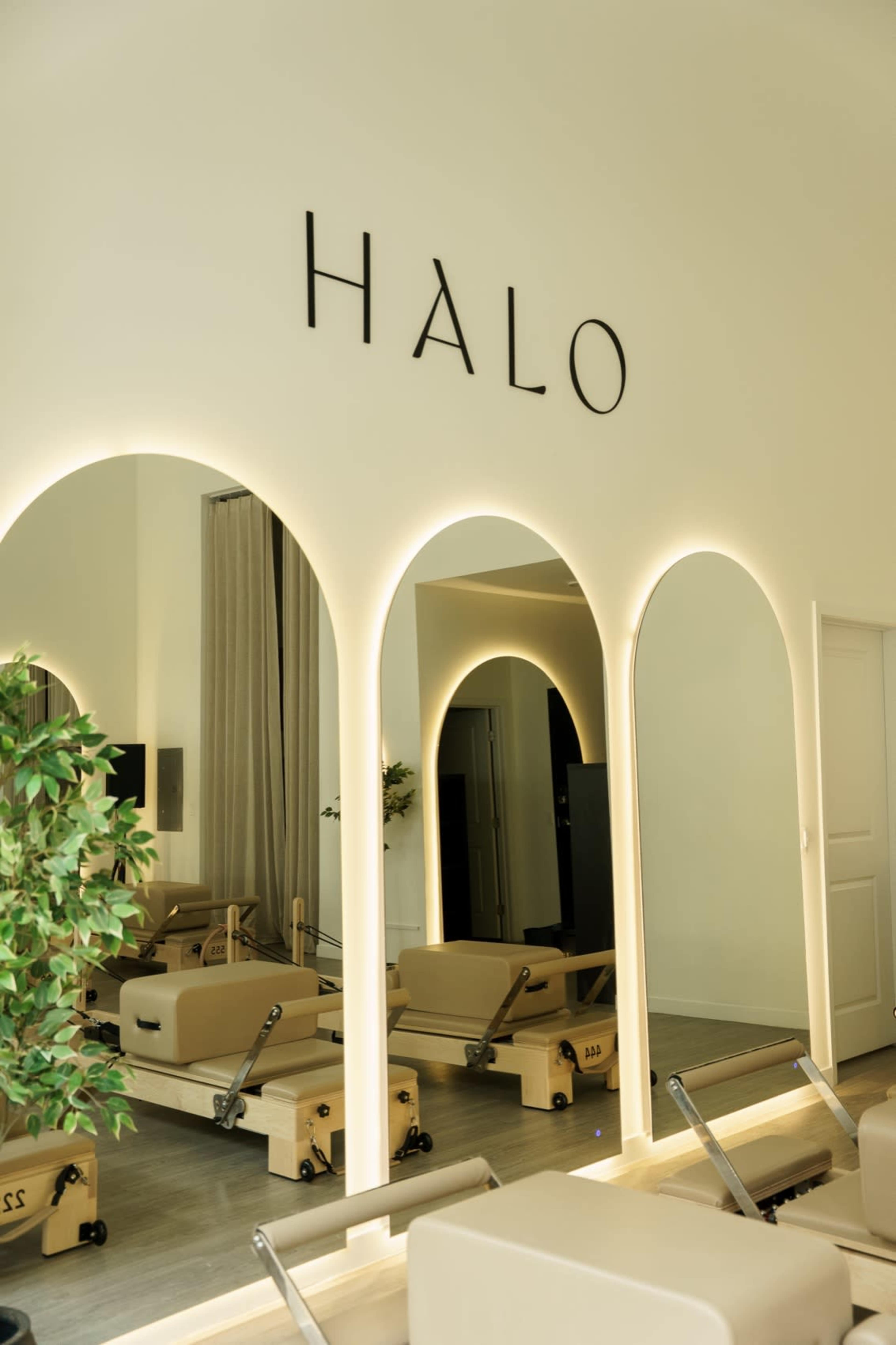 The image shows a modern fitness studio named "HALO" featuring three arched mirrors and reformer machines set against a light-colored wall.