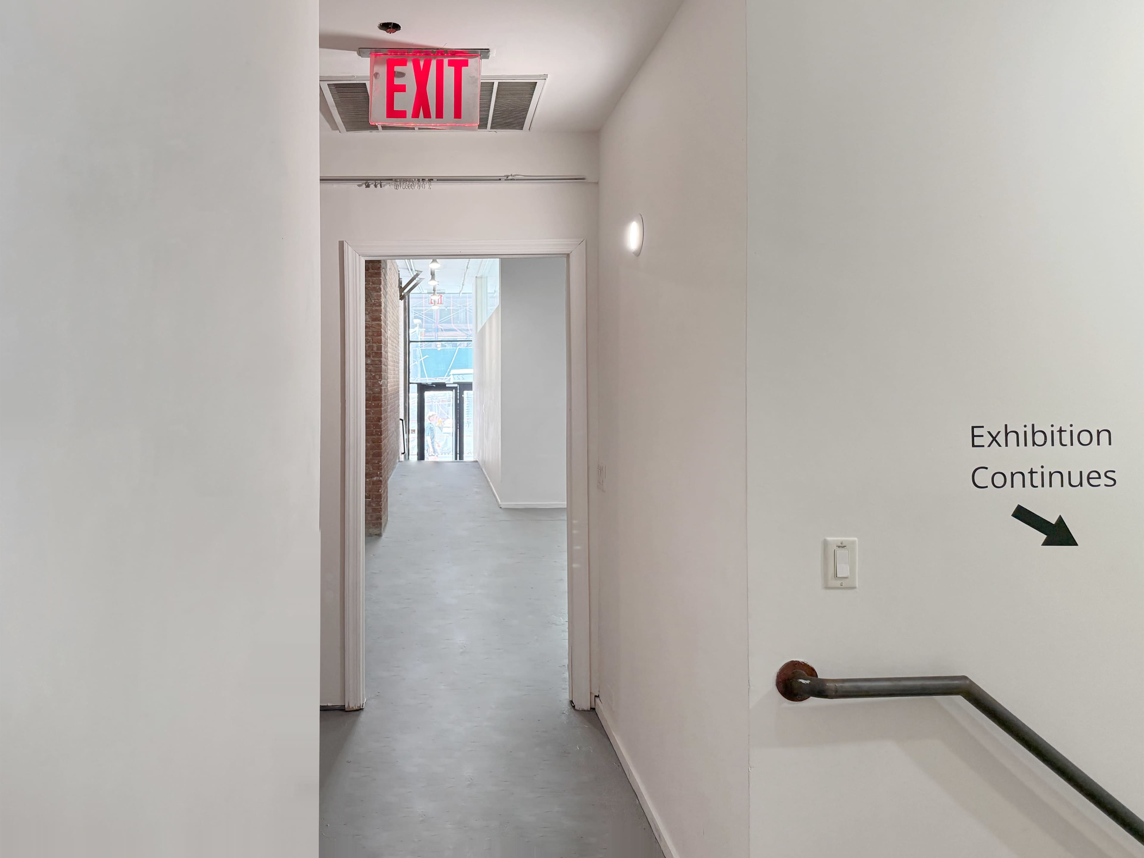 A well-lit corridor leads to a space with an exit sign and a directional arrow indicating that the exhibition continues.