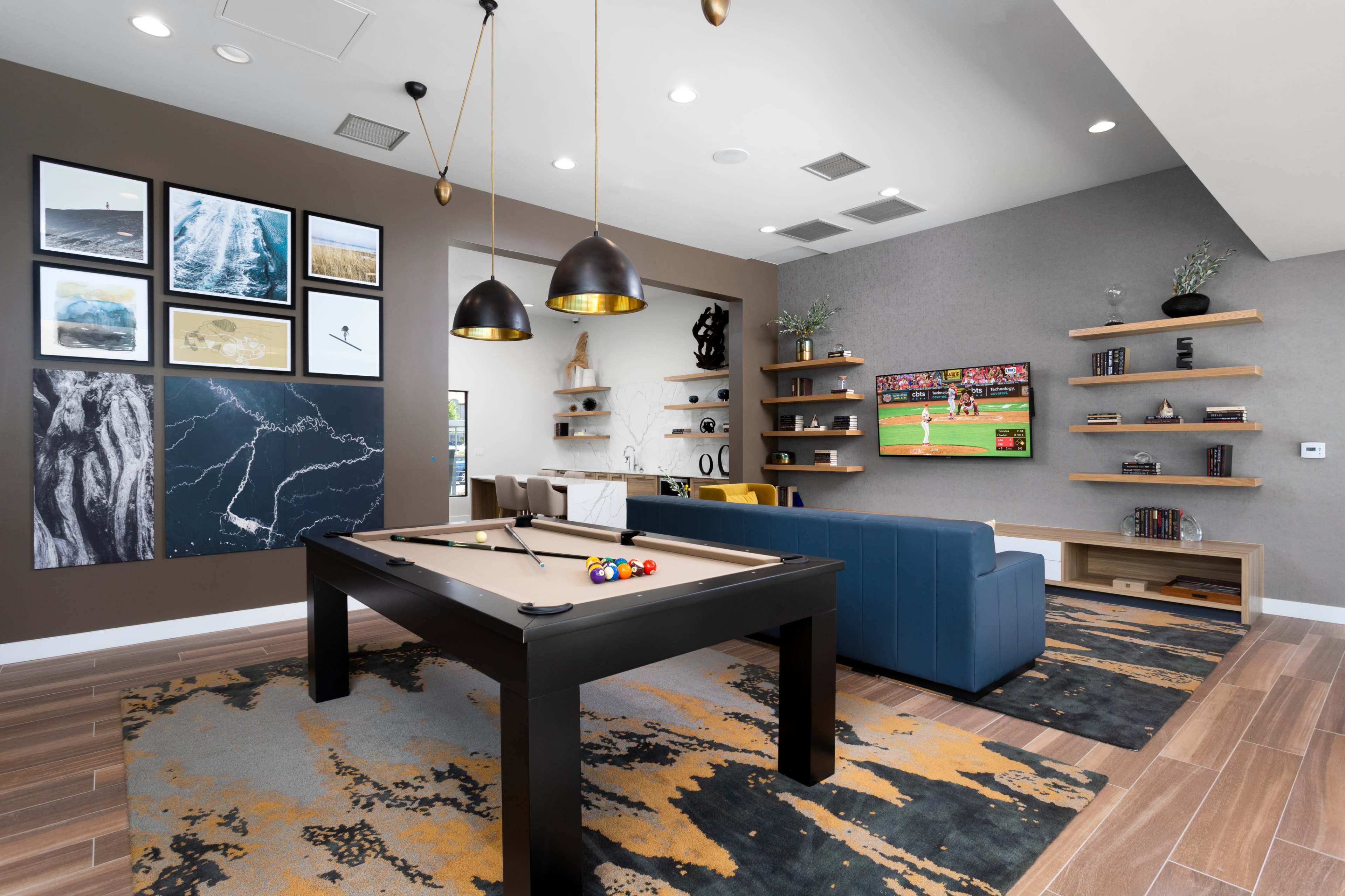 A modern game room featuring a pool table, a comfortable blue sofa, a wall-mounted TV displaying a sports game, and decorative artwork on the walls.