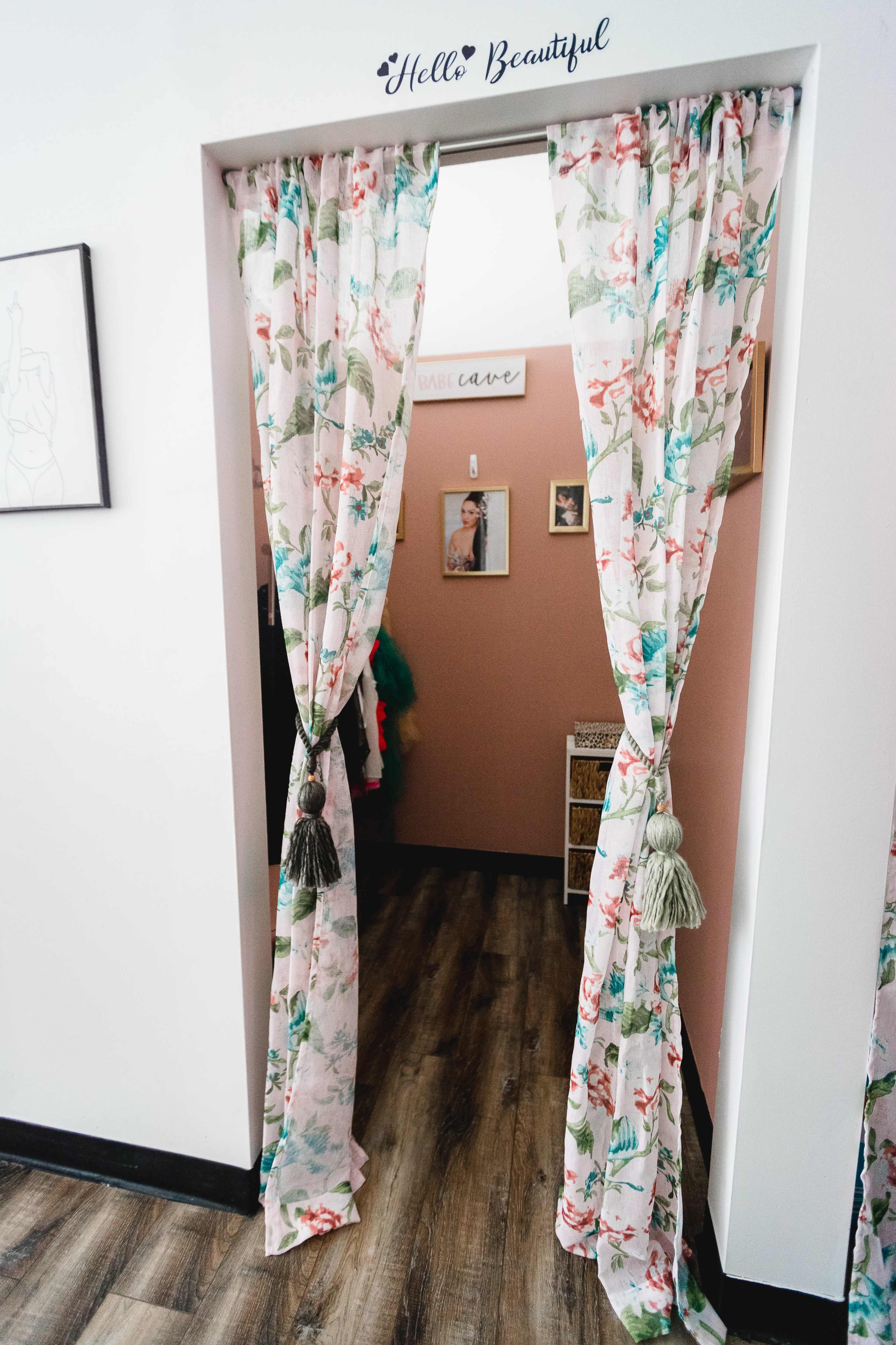 A set of floral curtains hangs in a doorway, leading to a room with pink walls and decorative items.
