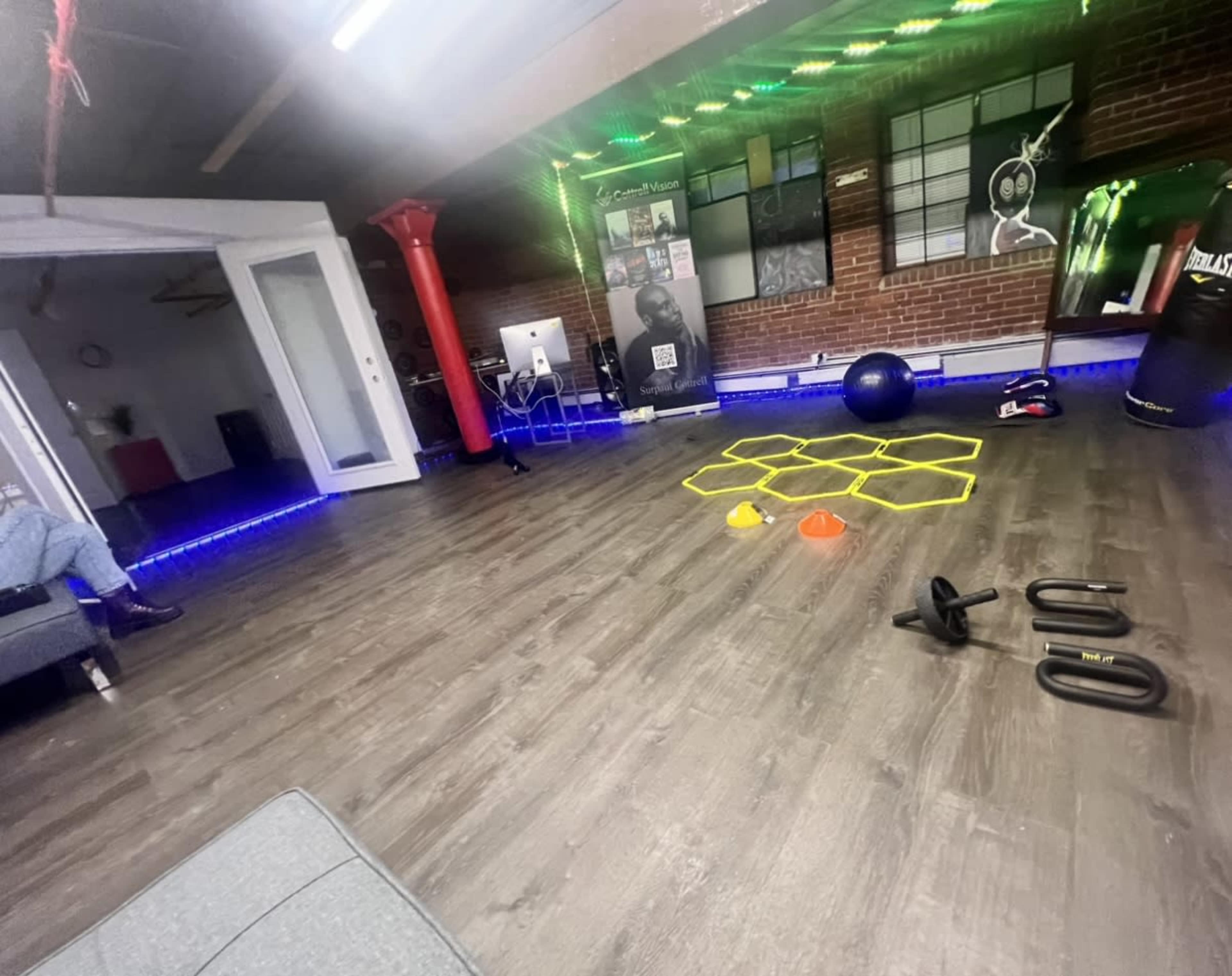 A fitness studio with exercise equipment, including weights, cones, and a stability ball, arranged on a wooden floor beneath colored lights.