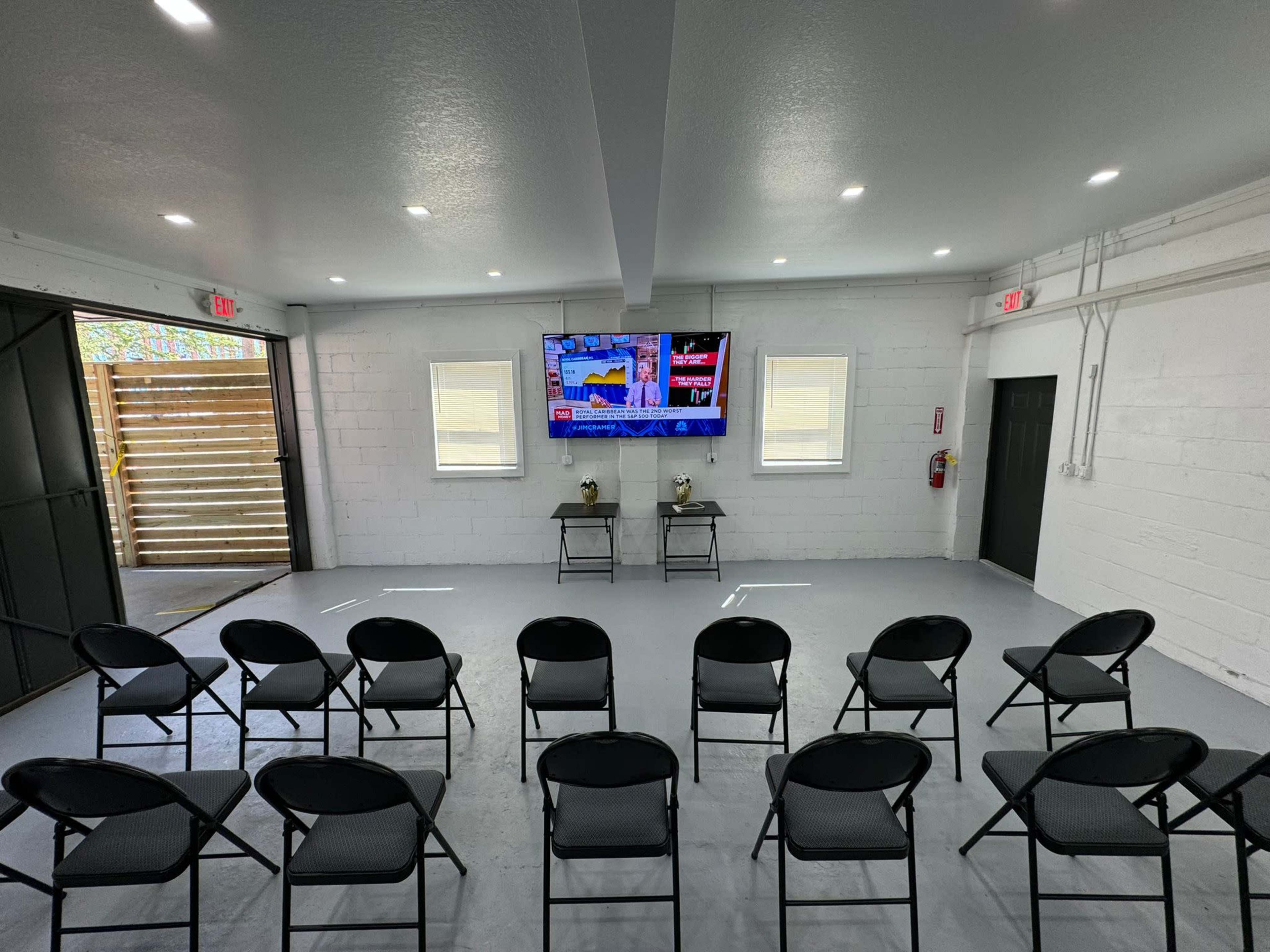 A spacious, well-lit room arranged with rows of black chairs facing a large TV mounted on the wall.