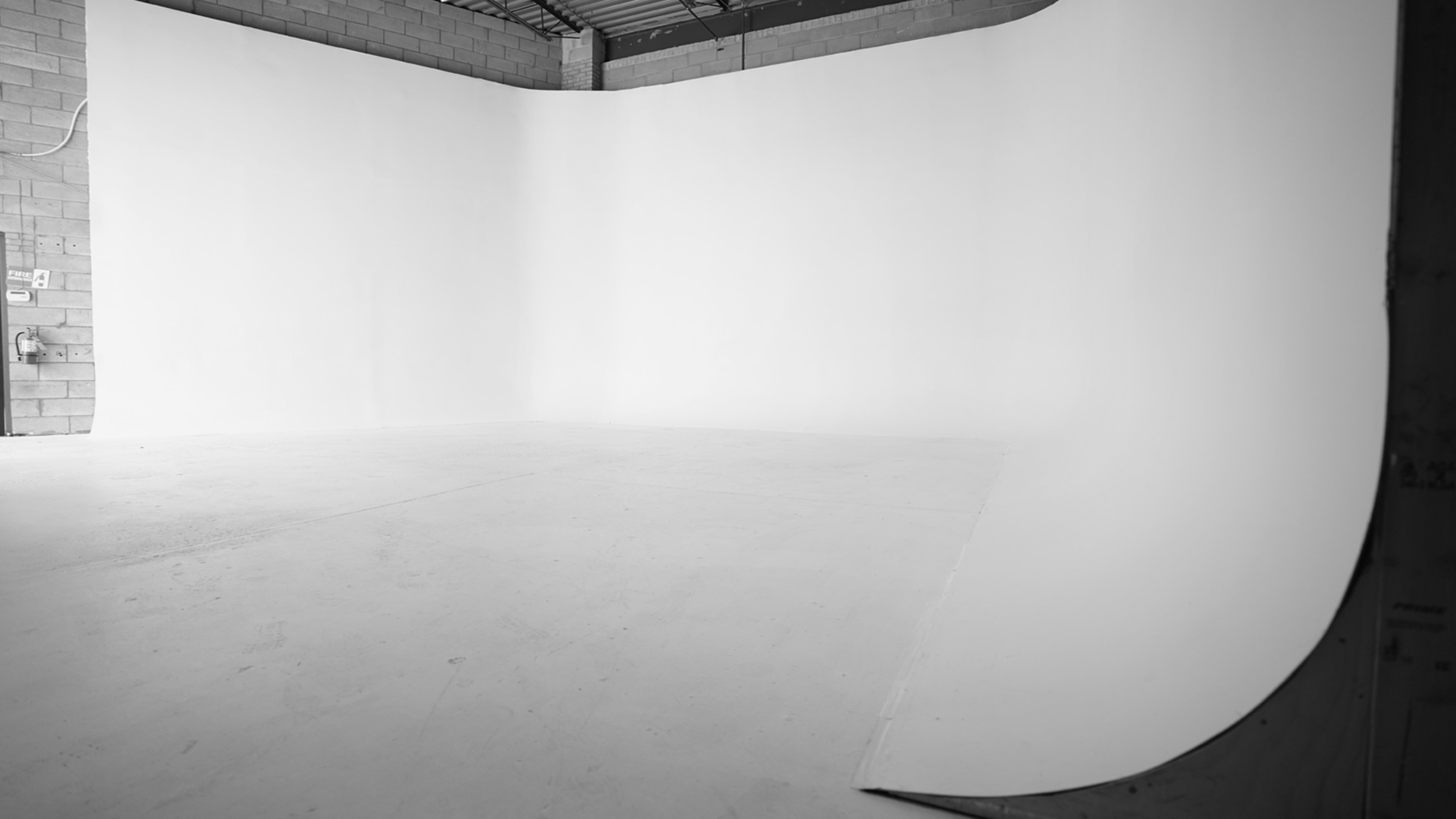 An empty photo studio with a seamless white backdrop and a smooth floor.