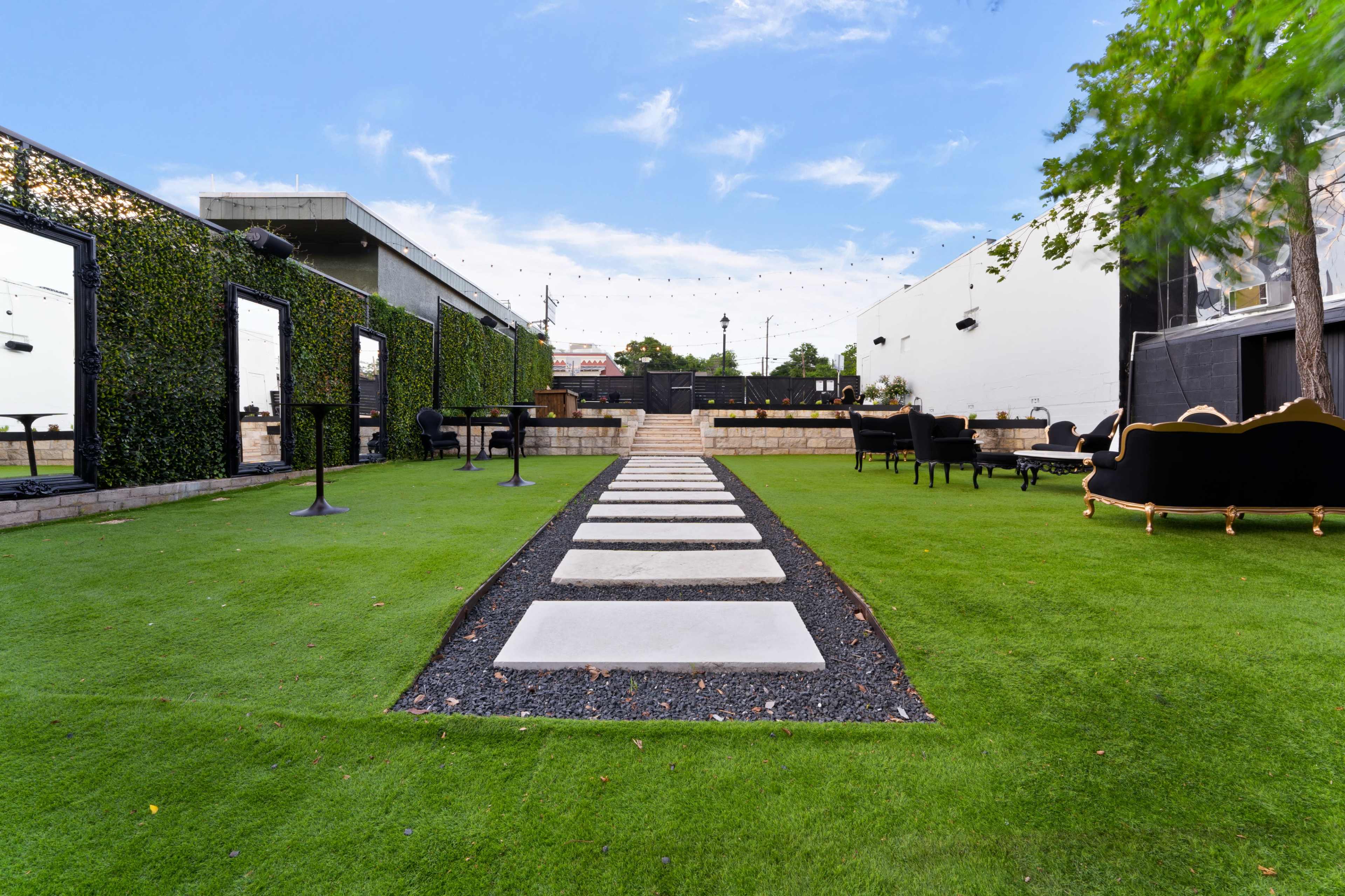A pathway of stone slabs leads through a green lawn, flanked by decorative walls and seating areas.