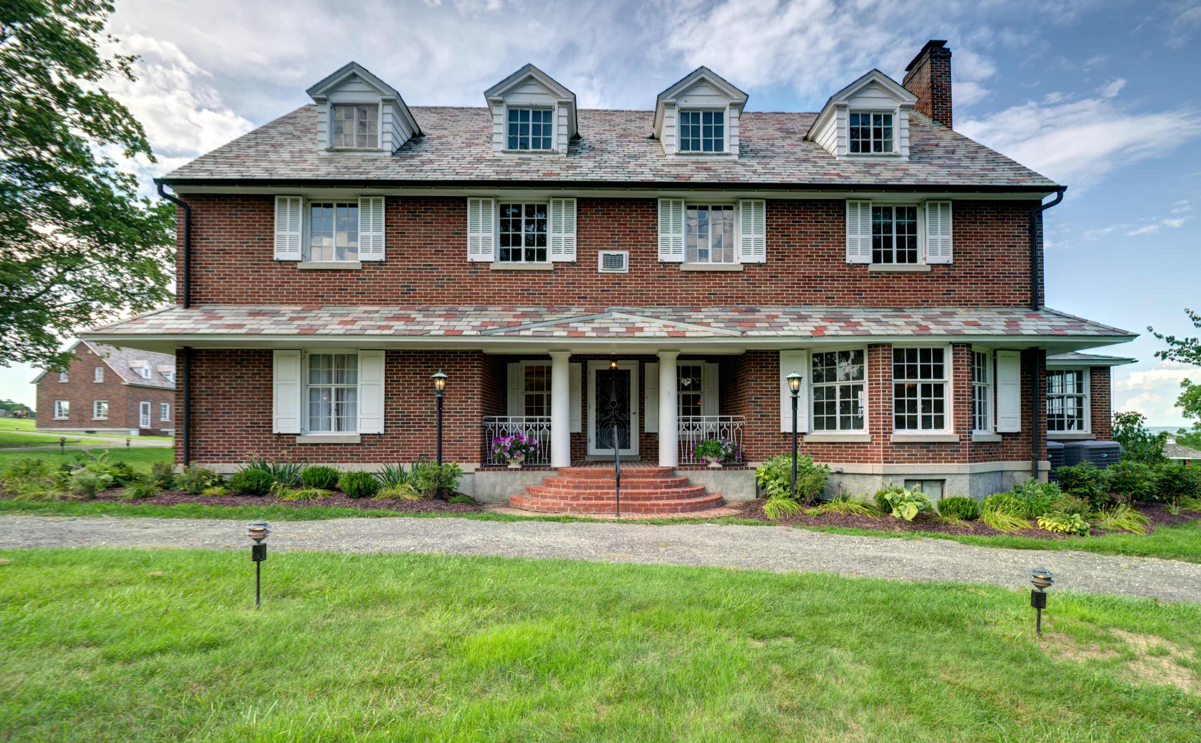 A large, two-and-a-half-story brick house with multiple gabled roofs, surrounded by a well-maintained lawn and pathway.