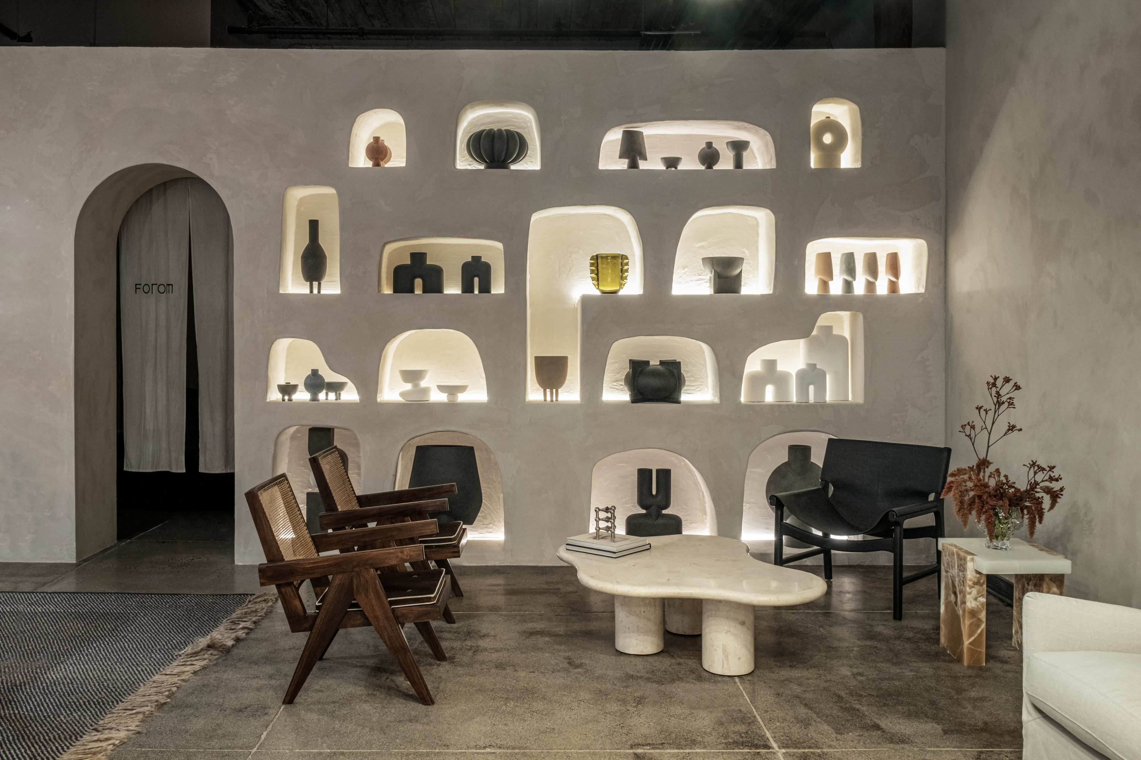 A modern interior space featuring a wall with illuminated shelves displaying various decorative vases and ceramics, along with minimalist furniture.