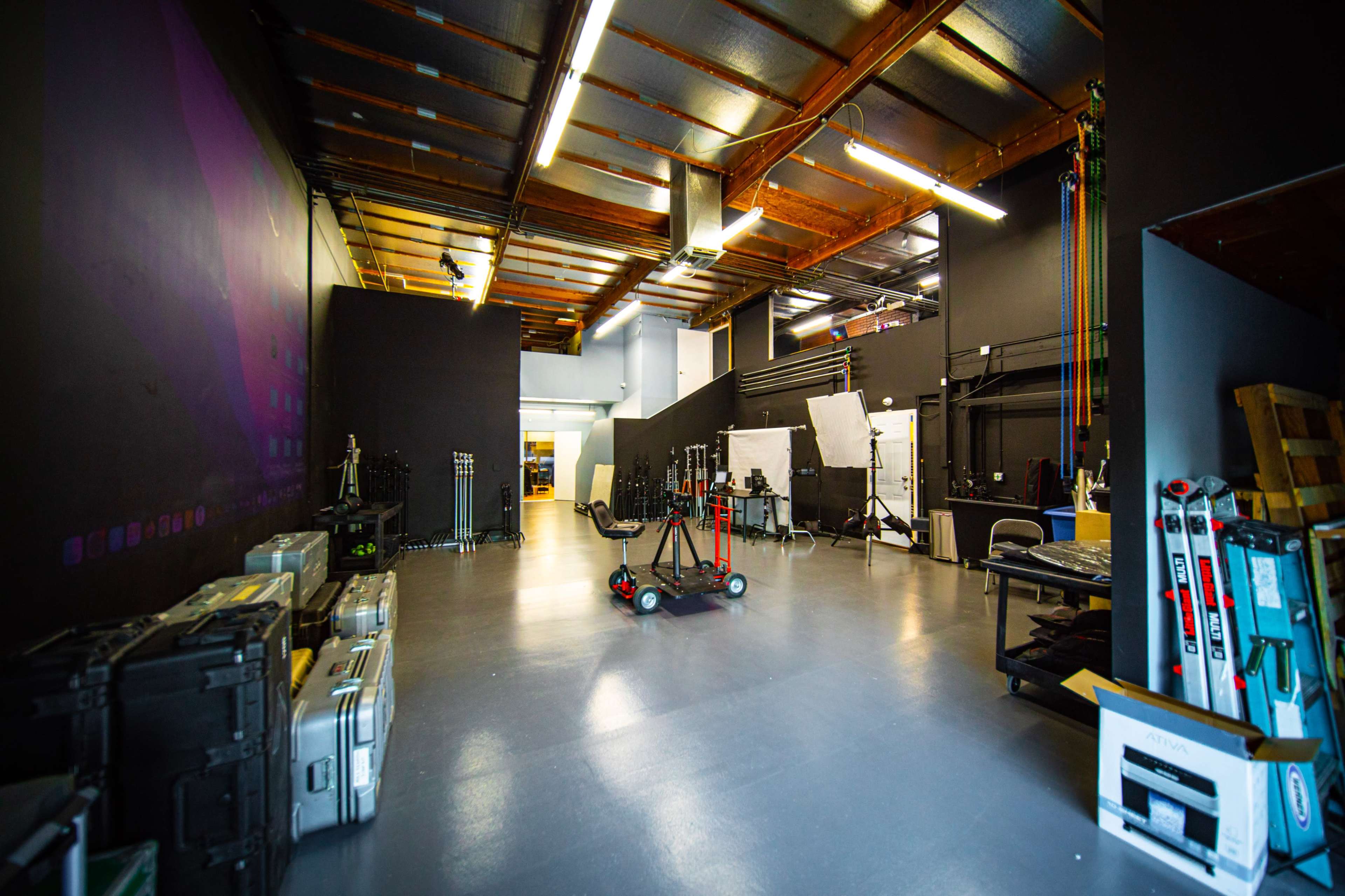 A spacious interior of a studio or workshop, featuring various equipment, lighting stands, and organized storage cases against the walls.
