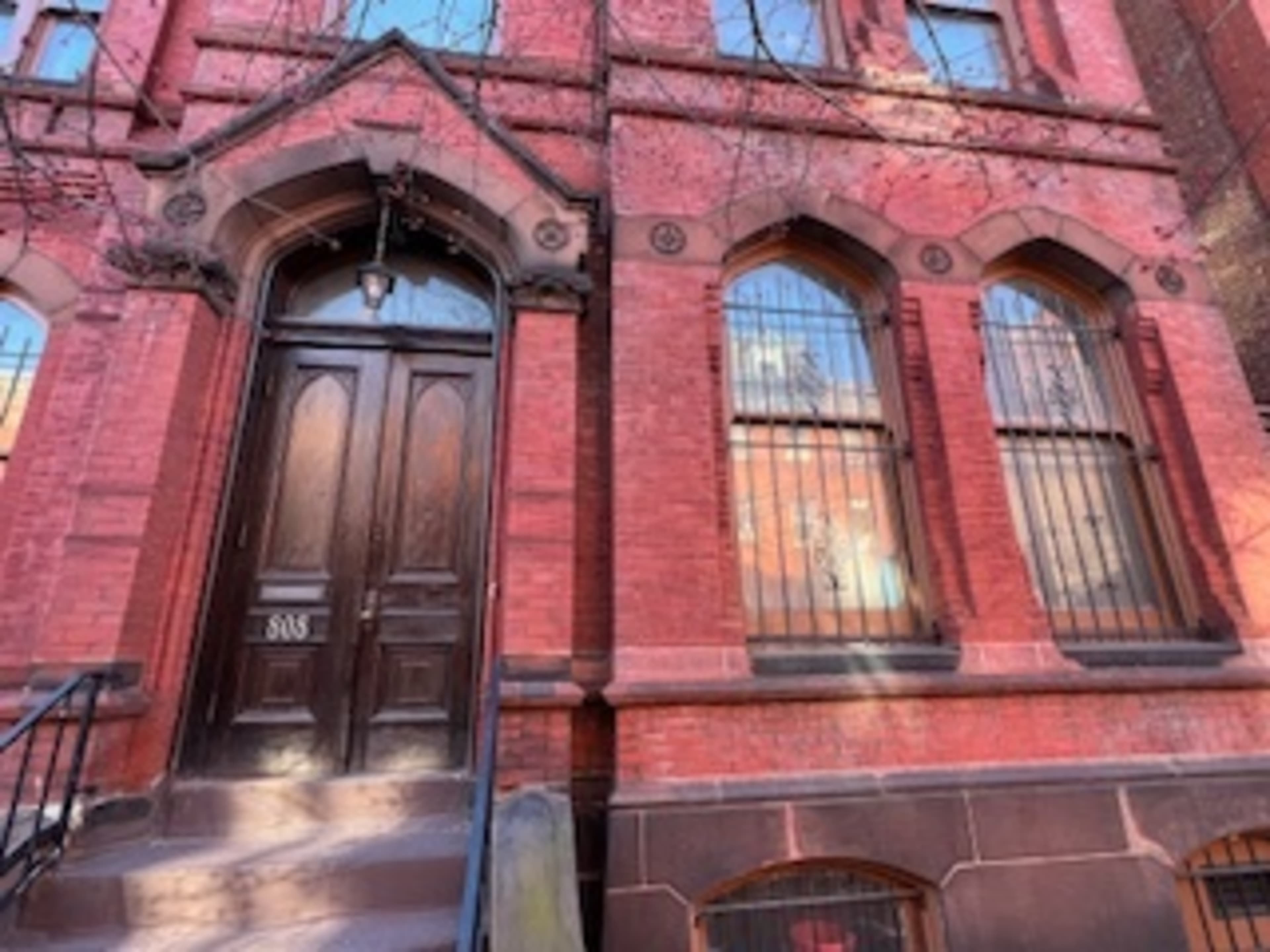 The entrance of a brick building with a wooden door and barred windows.