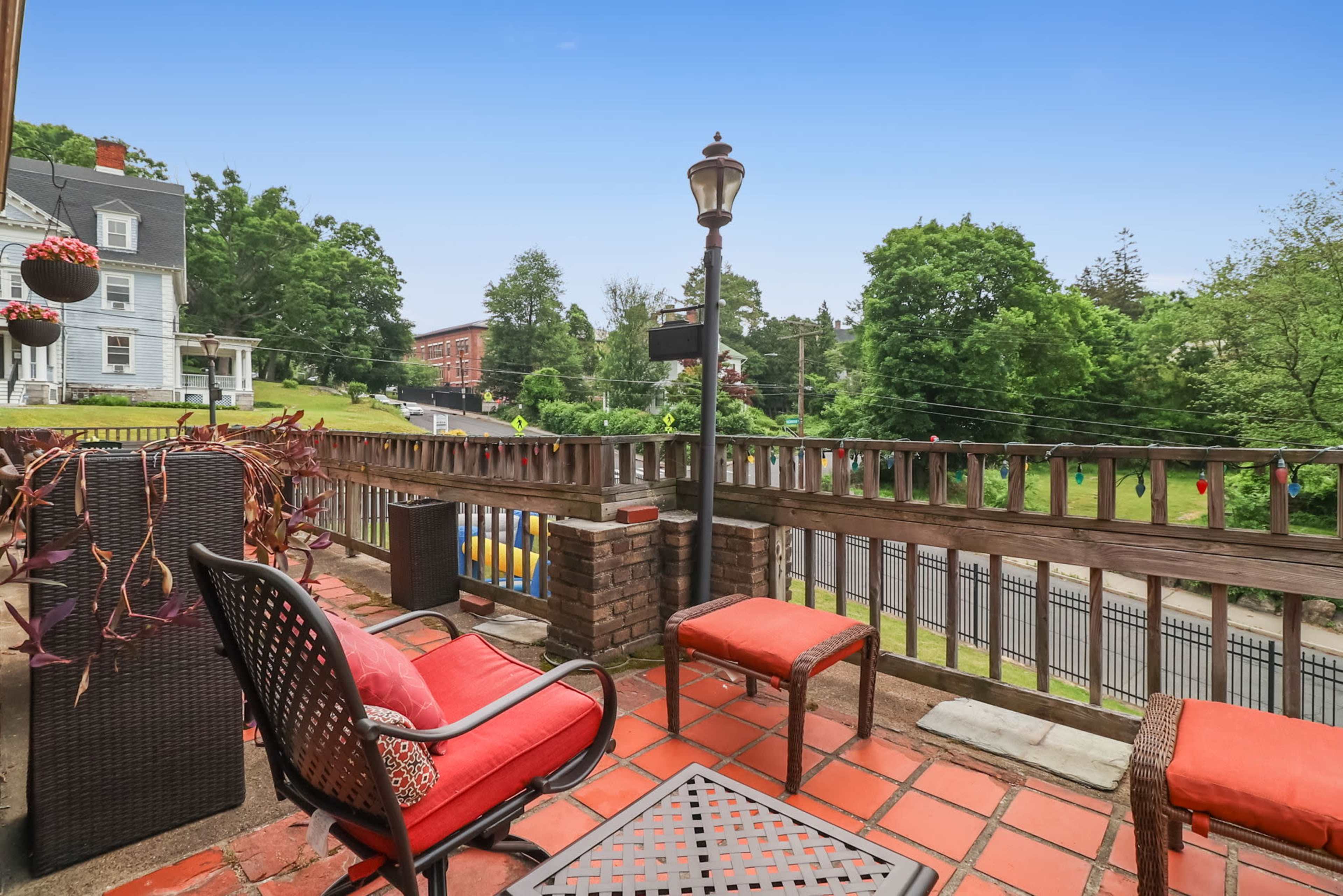 A patio area features a table and chairs, overlooking a green landscape with trees and a road in the background.