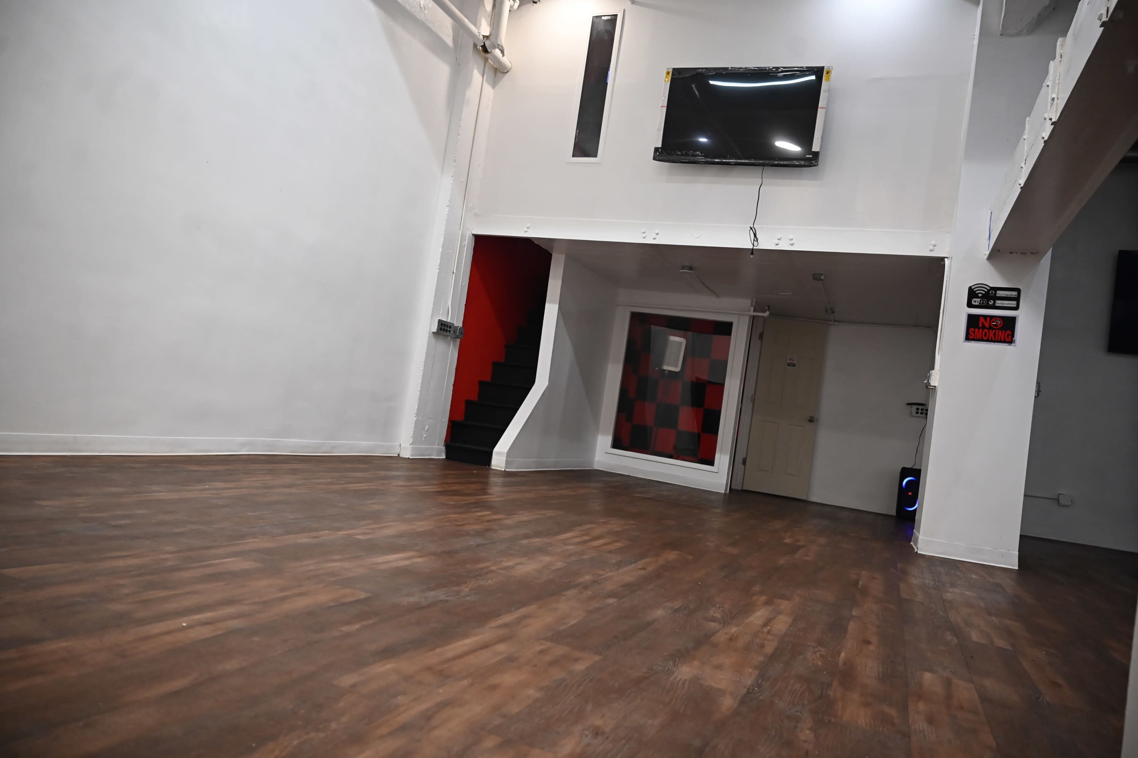 A spacious, empty room with wooden flooring, a staircase in the corner, and a television mounted on the wall.