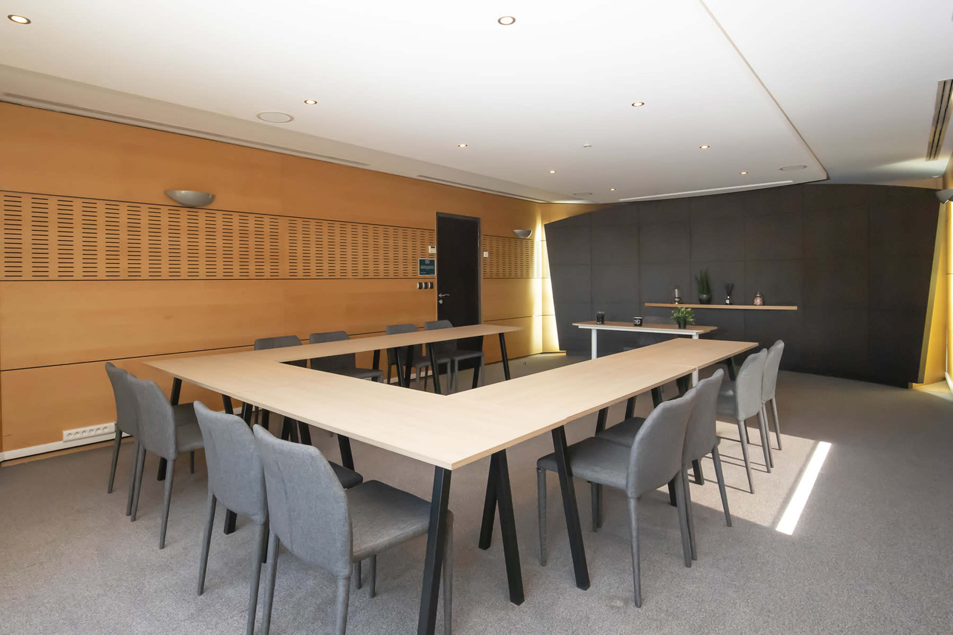A conference room with a large, rectangular table surrounded by chairs, and a black wall with decorative elements at the end of the room.