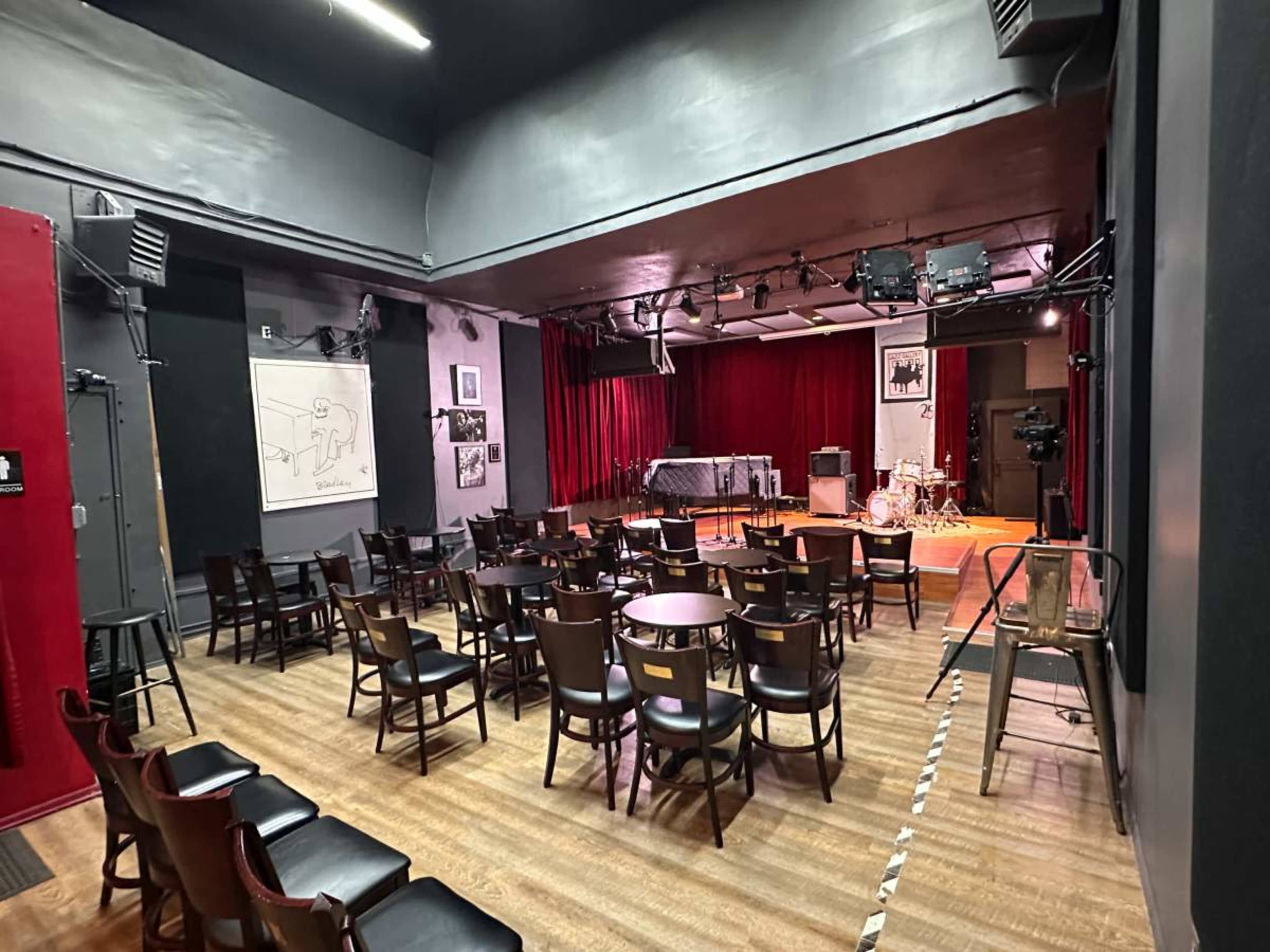 A small performance venue with rows of chairs facing a small stage, adorned with red curtains and various musical equipment.