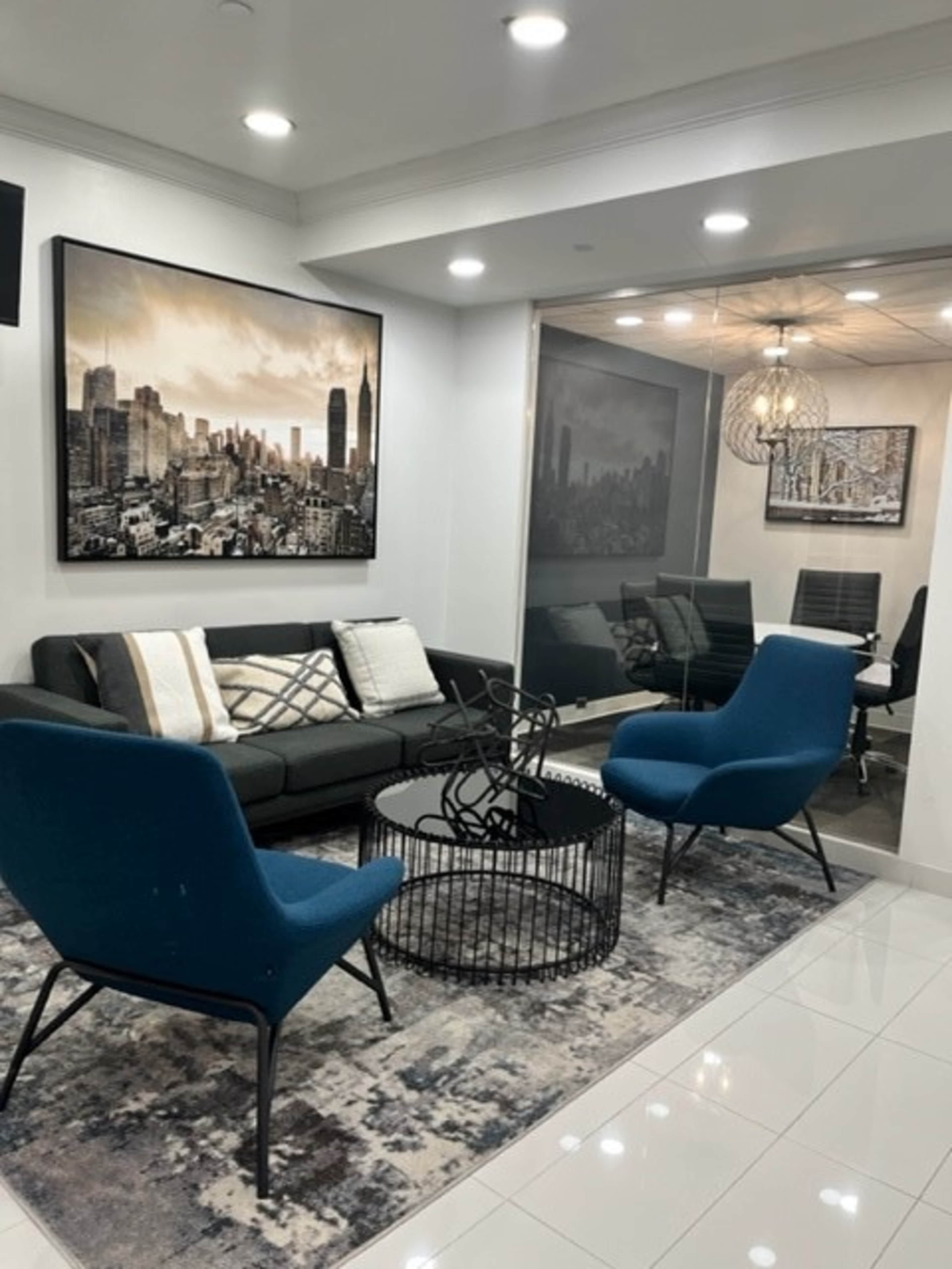 A modern lounge area with a black sofa, two blue armchairs, a circular coffee table, and a large cityscape artwork on the wall.