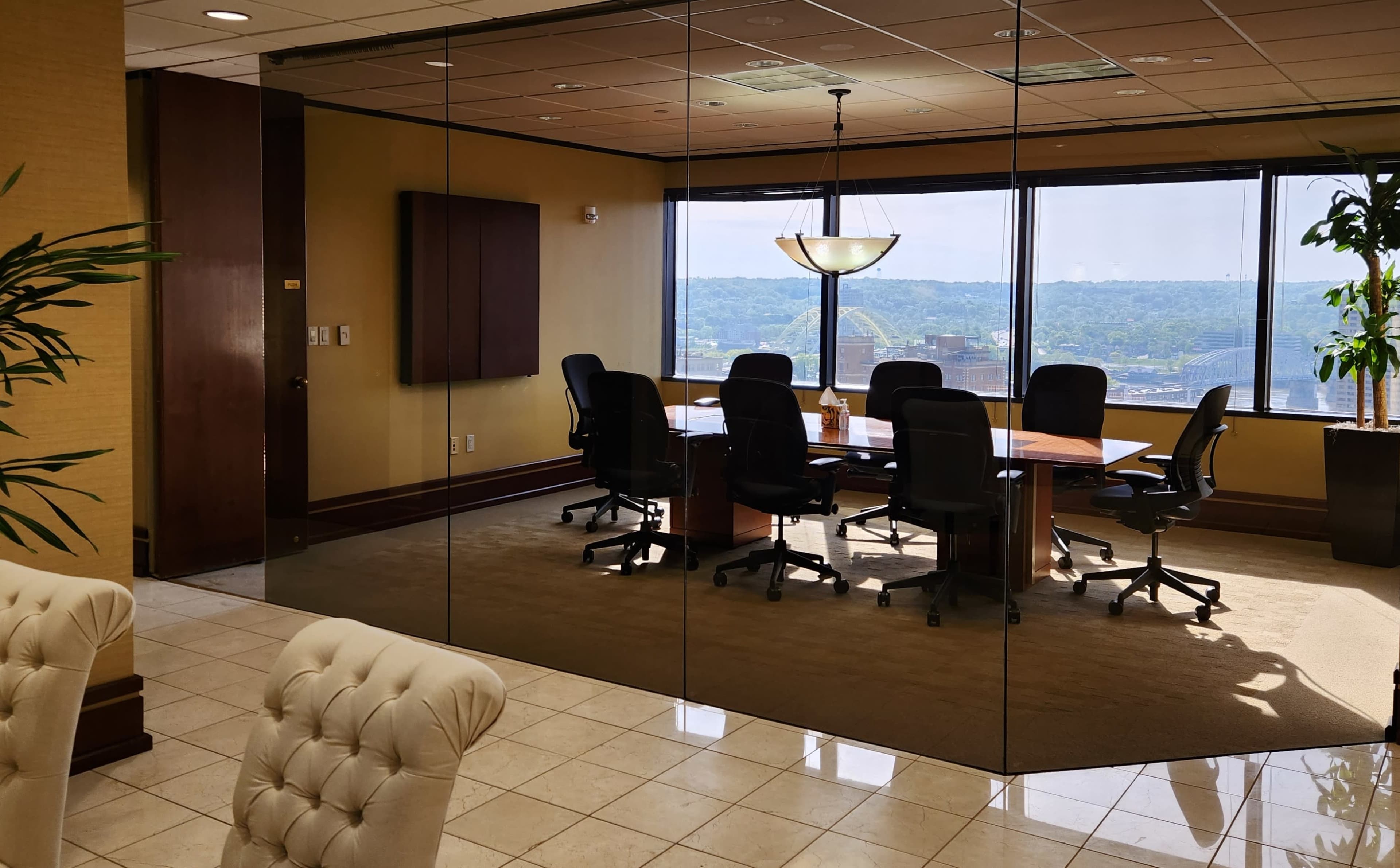 A glass-walled conference room with a large table and chairs overlooks a view of a landscape through large windows.