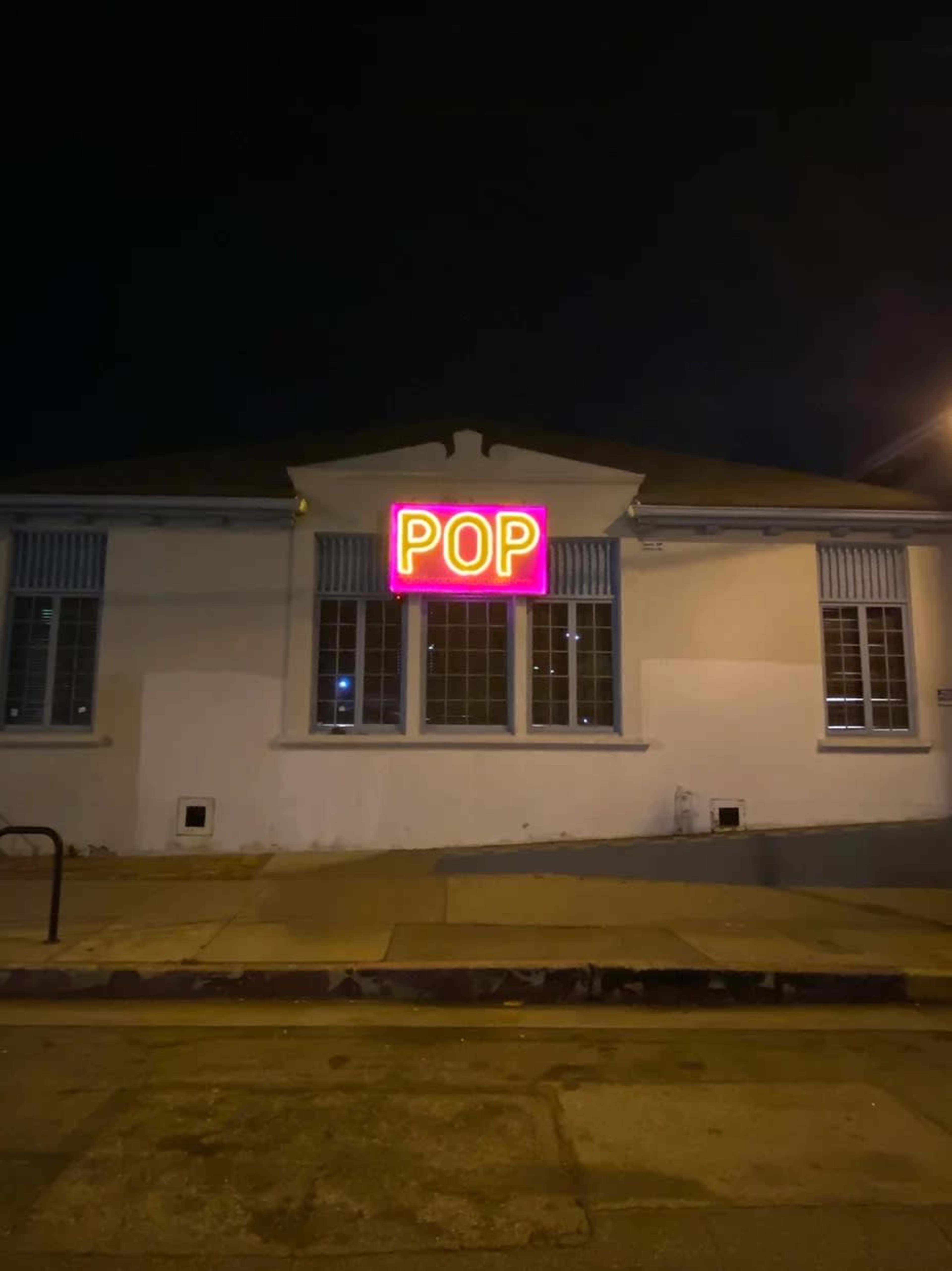 A building at night features a brightly lit neon sign displaying the word "POP."