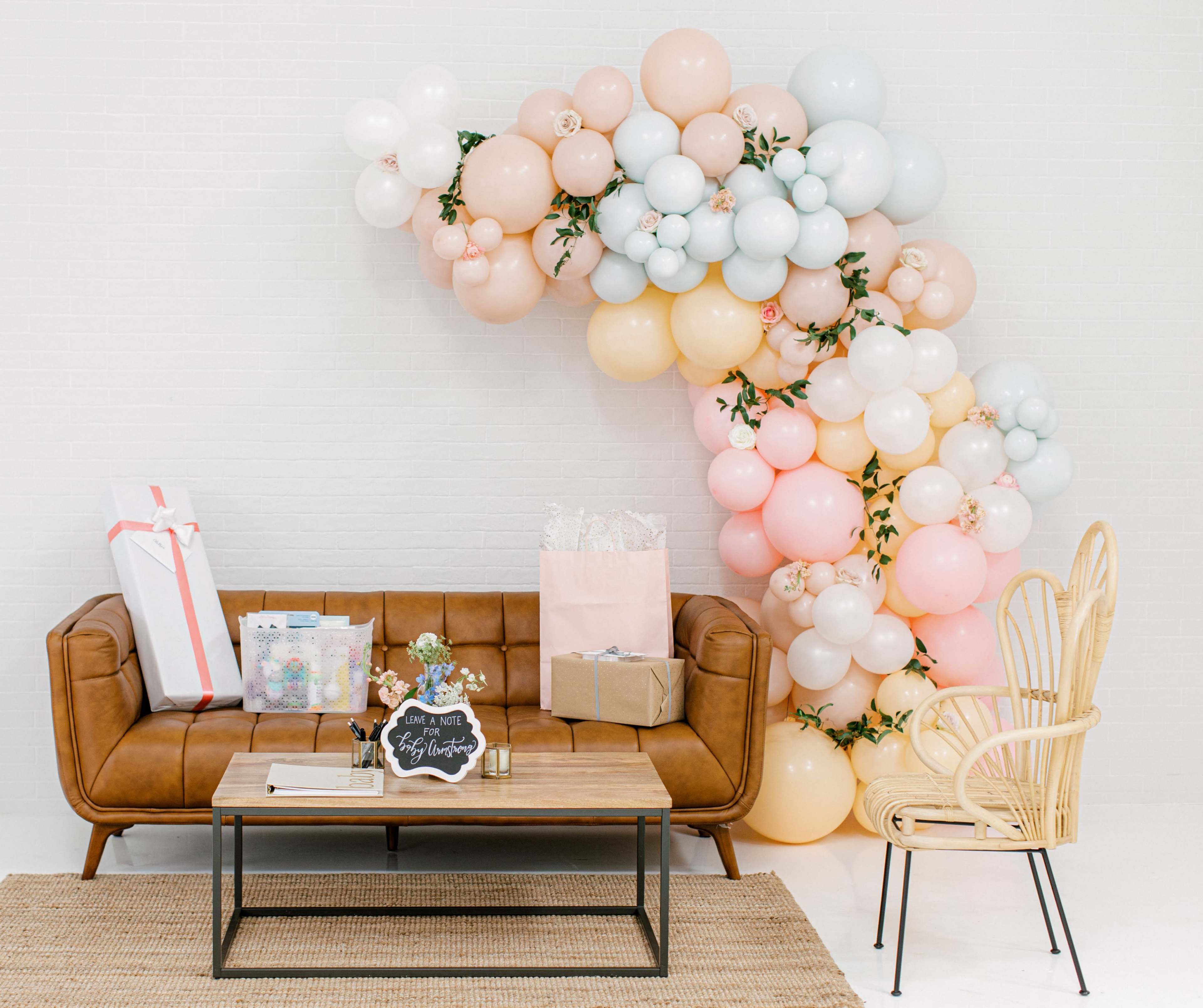 A brown leather sofa is positioned in front of a table, with a colorful balloon arch and gift packages on the floor beside it.