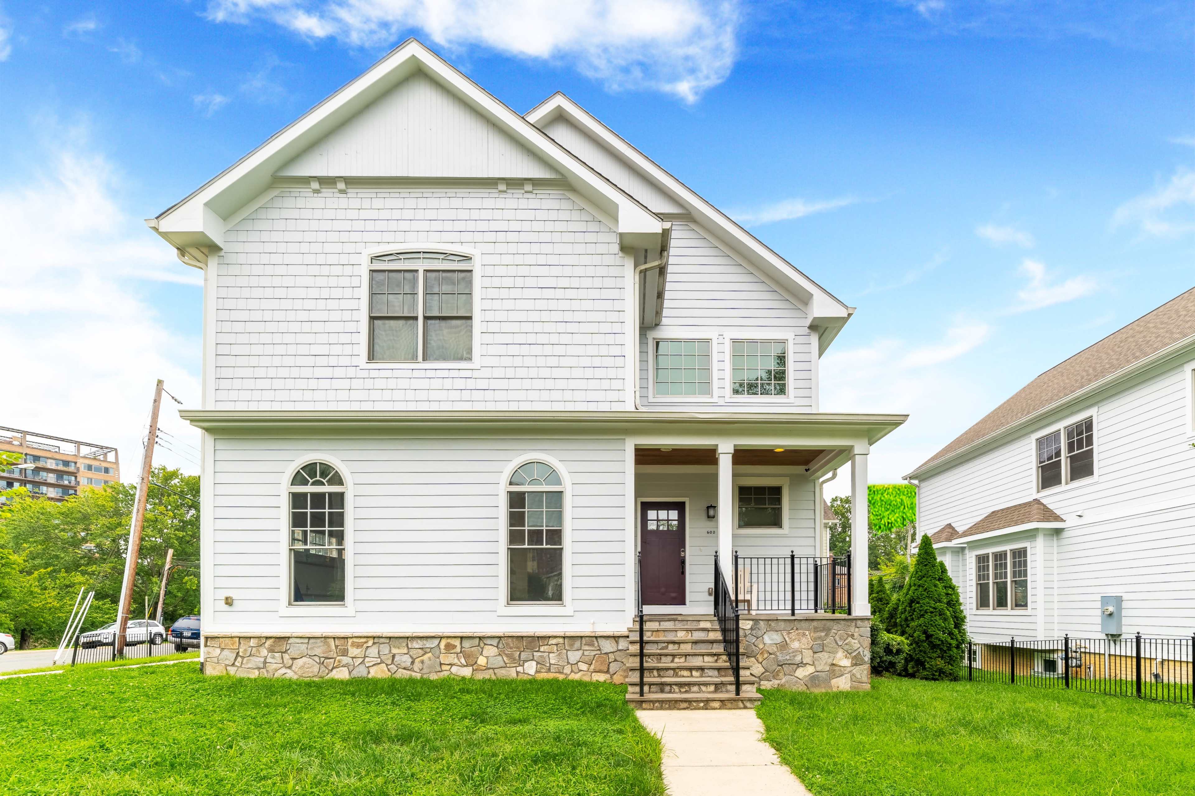 A two-story, white house with a stone base, a front porch, and green grass in the yard.