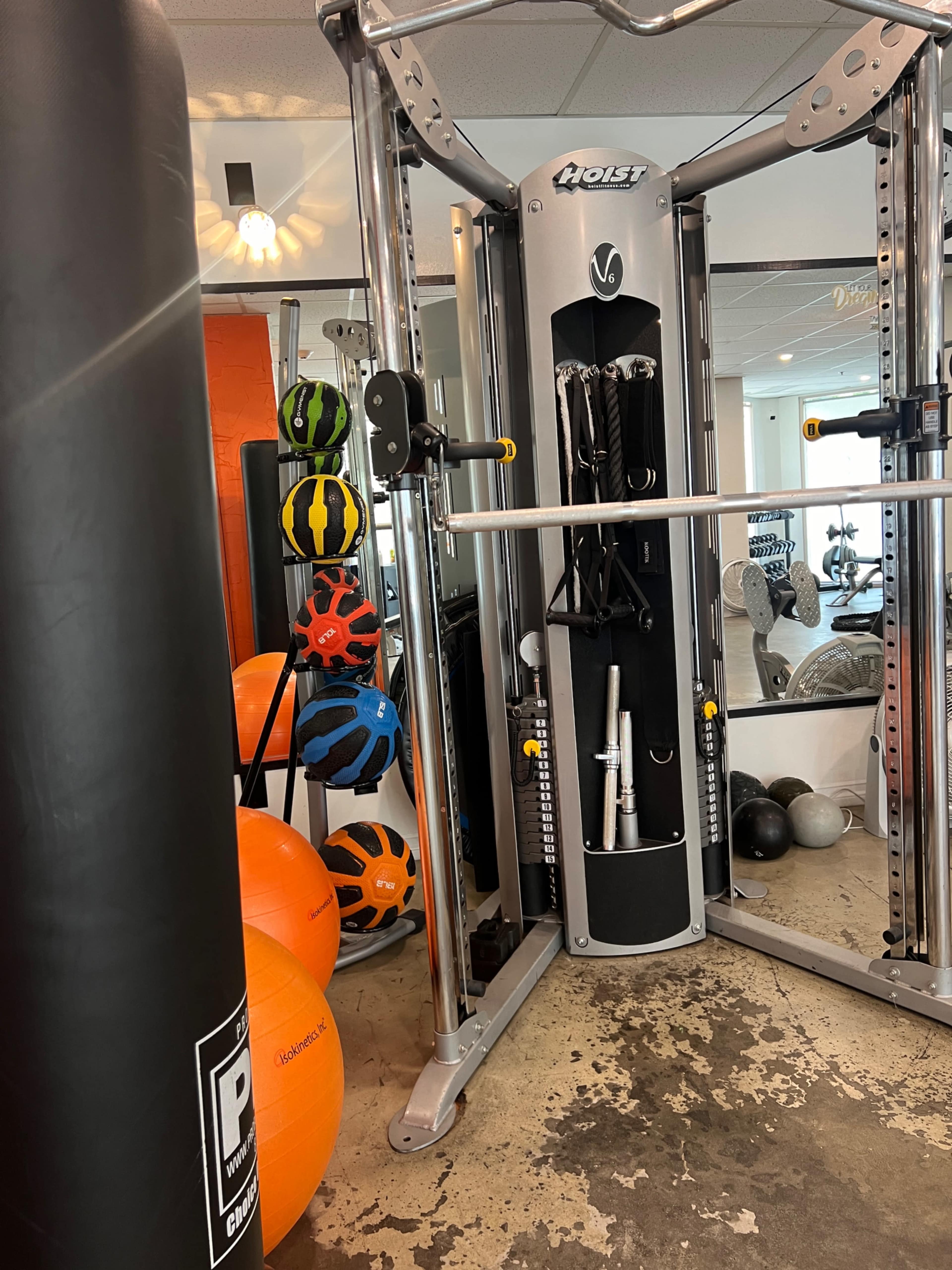 The image shows a gym area featuring a cable machine, exercise balls, a punching bag, and various weights.