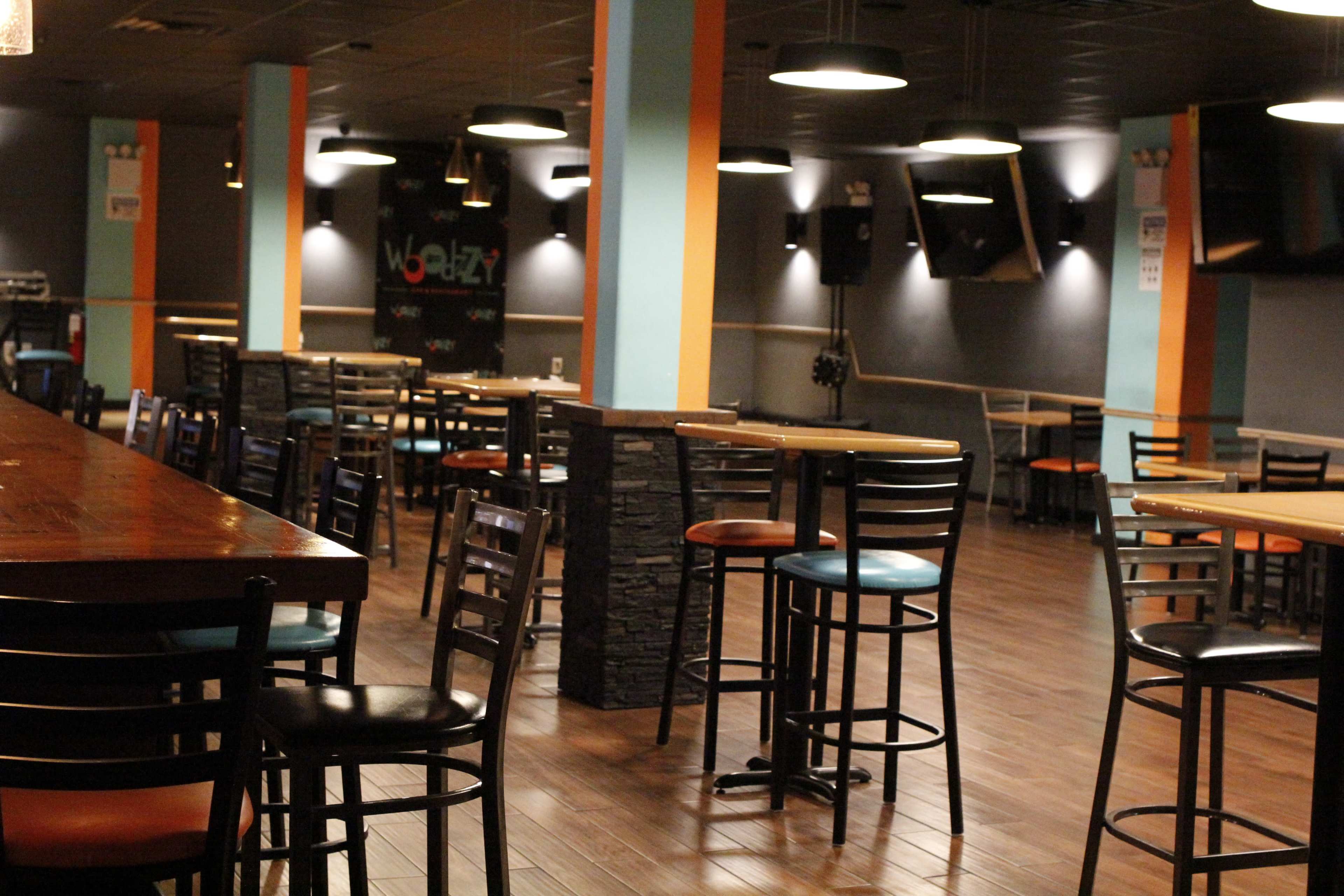 An empty bar area with wooden tables and black chairs arranged in a spacious, well-lit setting.