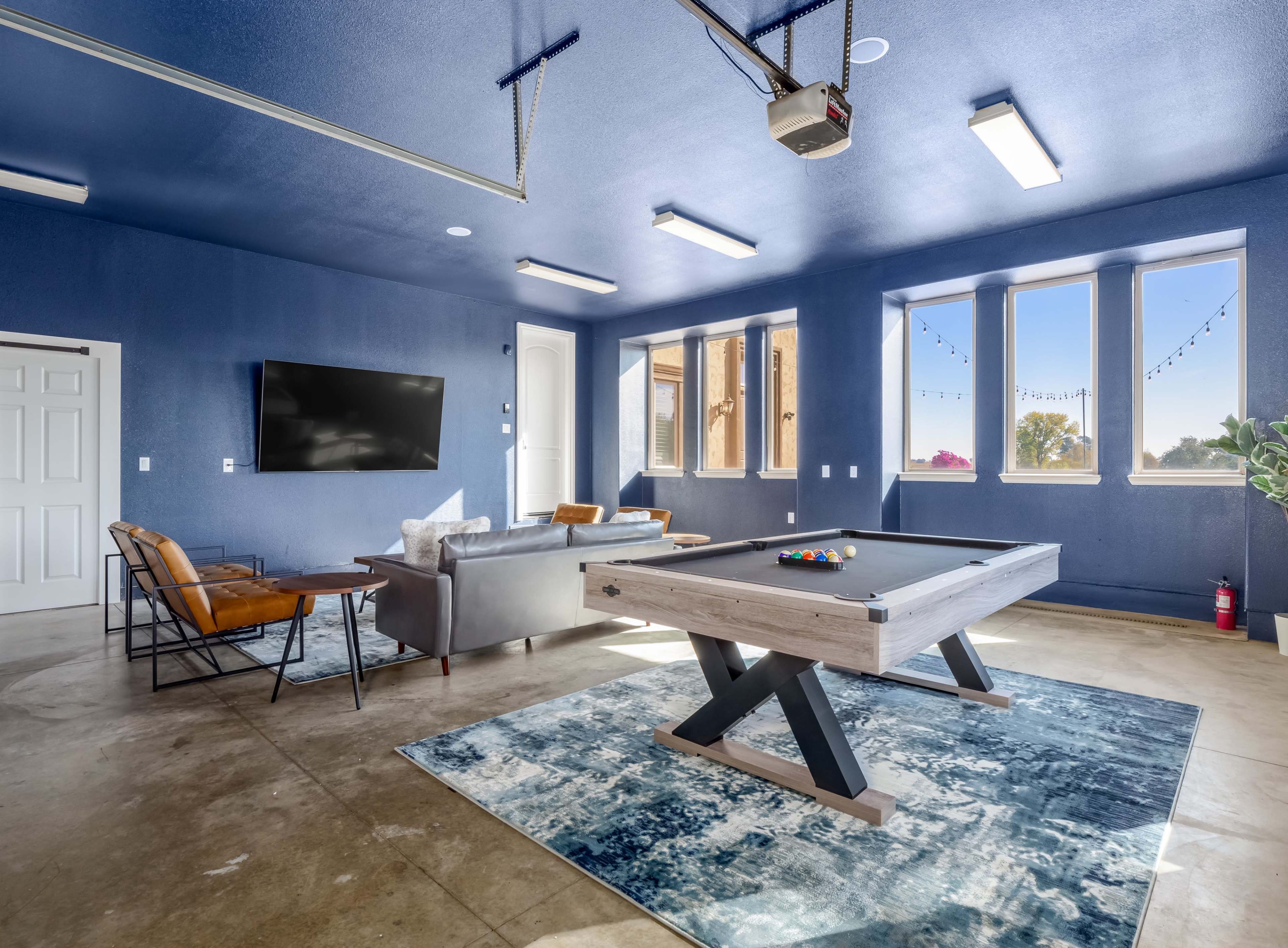 A spacious garage converted into a recreational room, featuring a pool table, seating area, and large windows.
