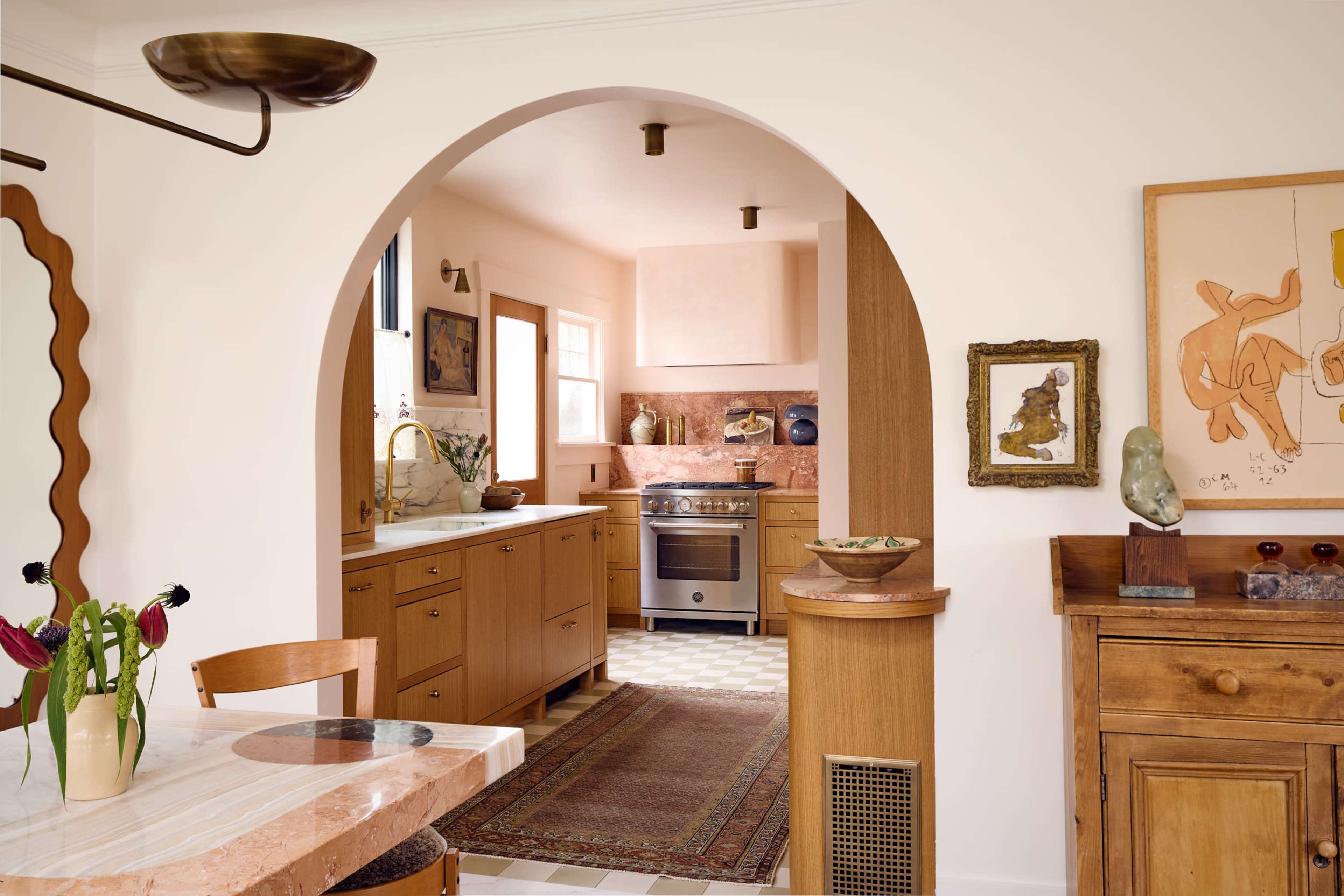 A hallway with an archway leads to a kitchen featuring wooden cabinetry, a stove, and a patterned floor.