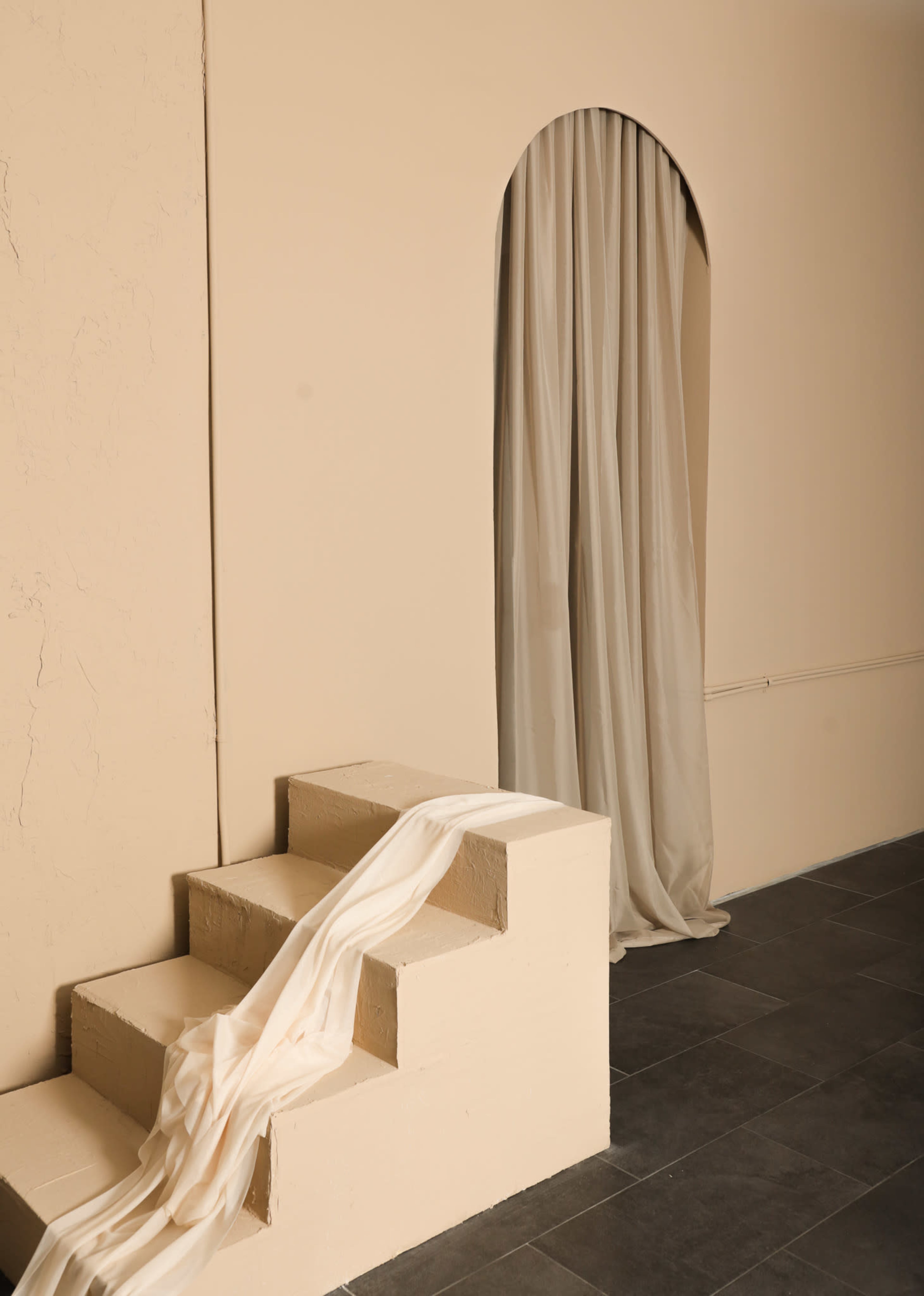 A set of three steps leads to an arched opening draped with a light-colored curtain against a pale wall.