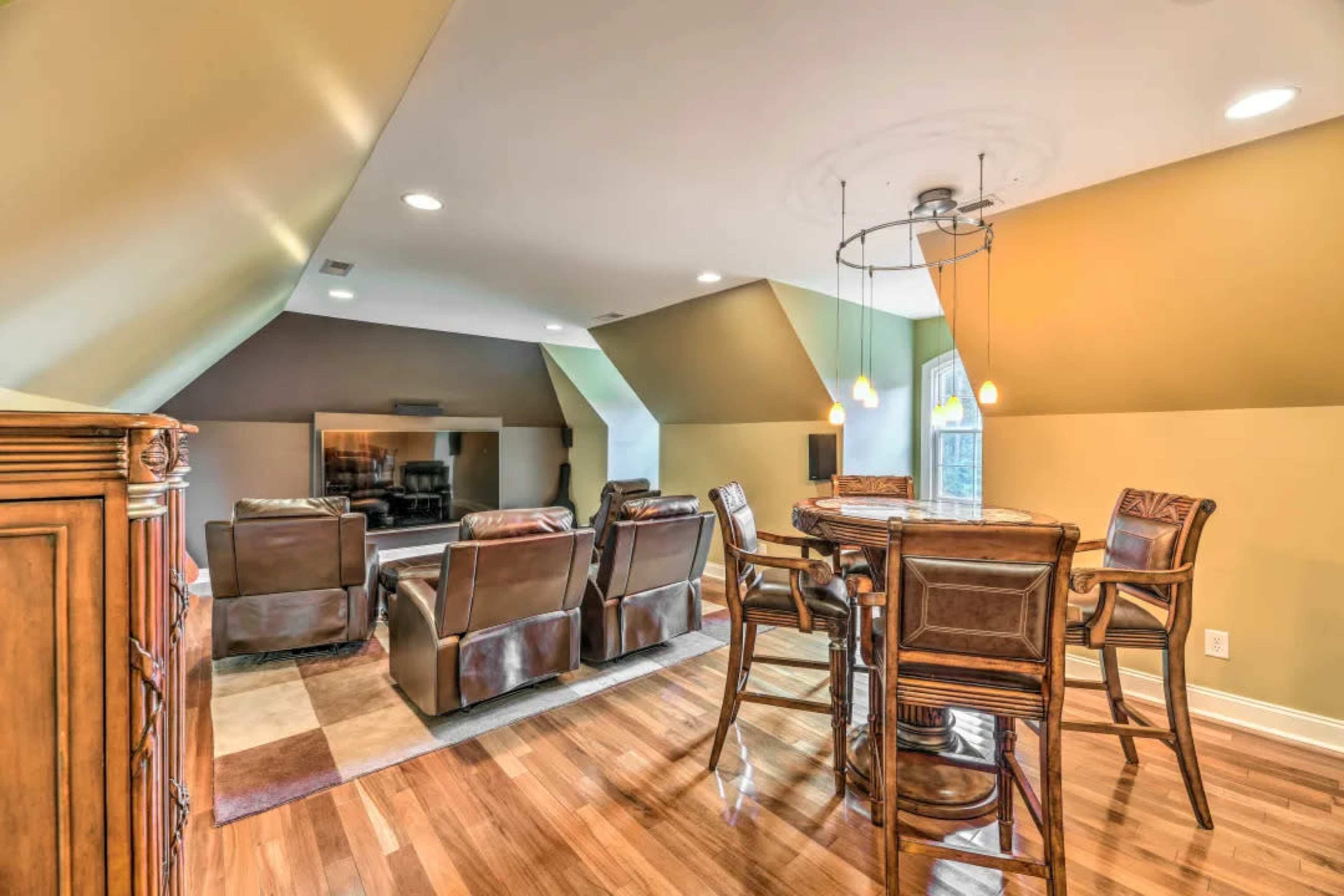 A spacious attic room with a seating area, dining table, and large windows.