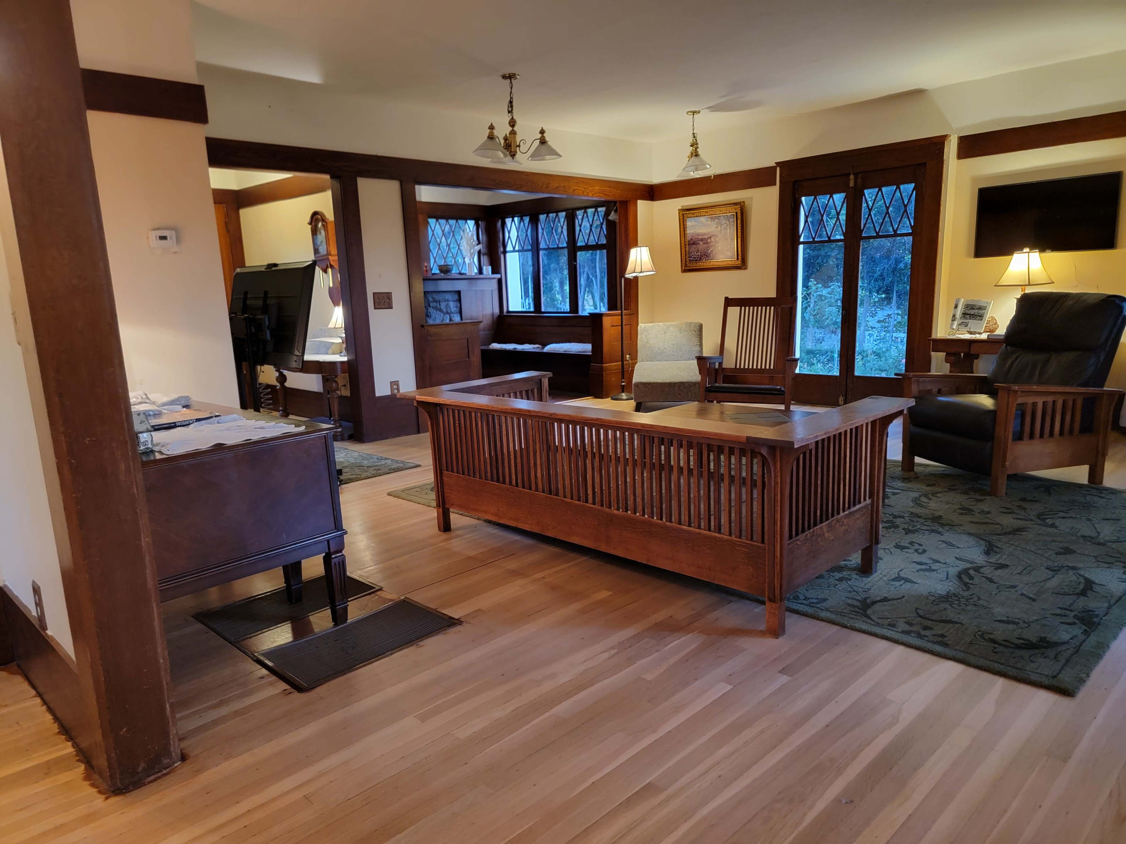 The image shows a cozy living room with wooden furniture, a coffee table in the center, and windows allowing natural light to enter.