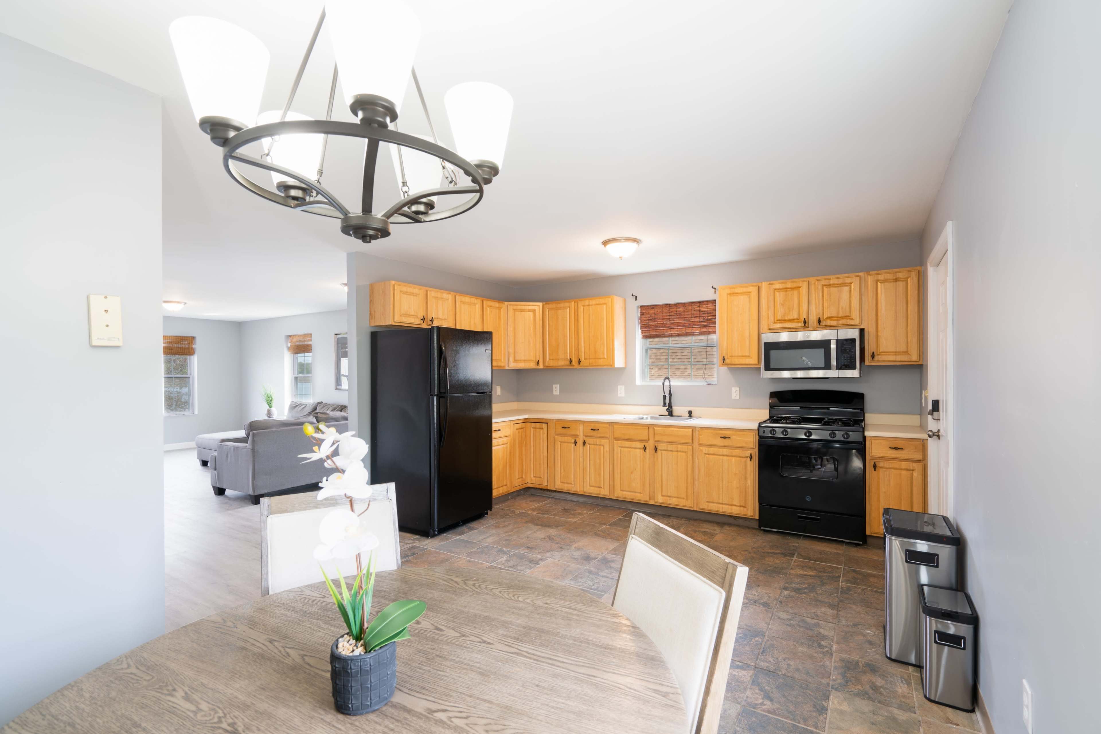 A kitchen with wooden cabinets, a black refrigerator, a stainless steel microwave, and a dining table with a plant centerpiece.