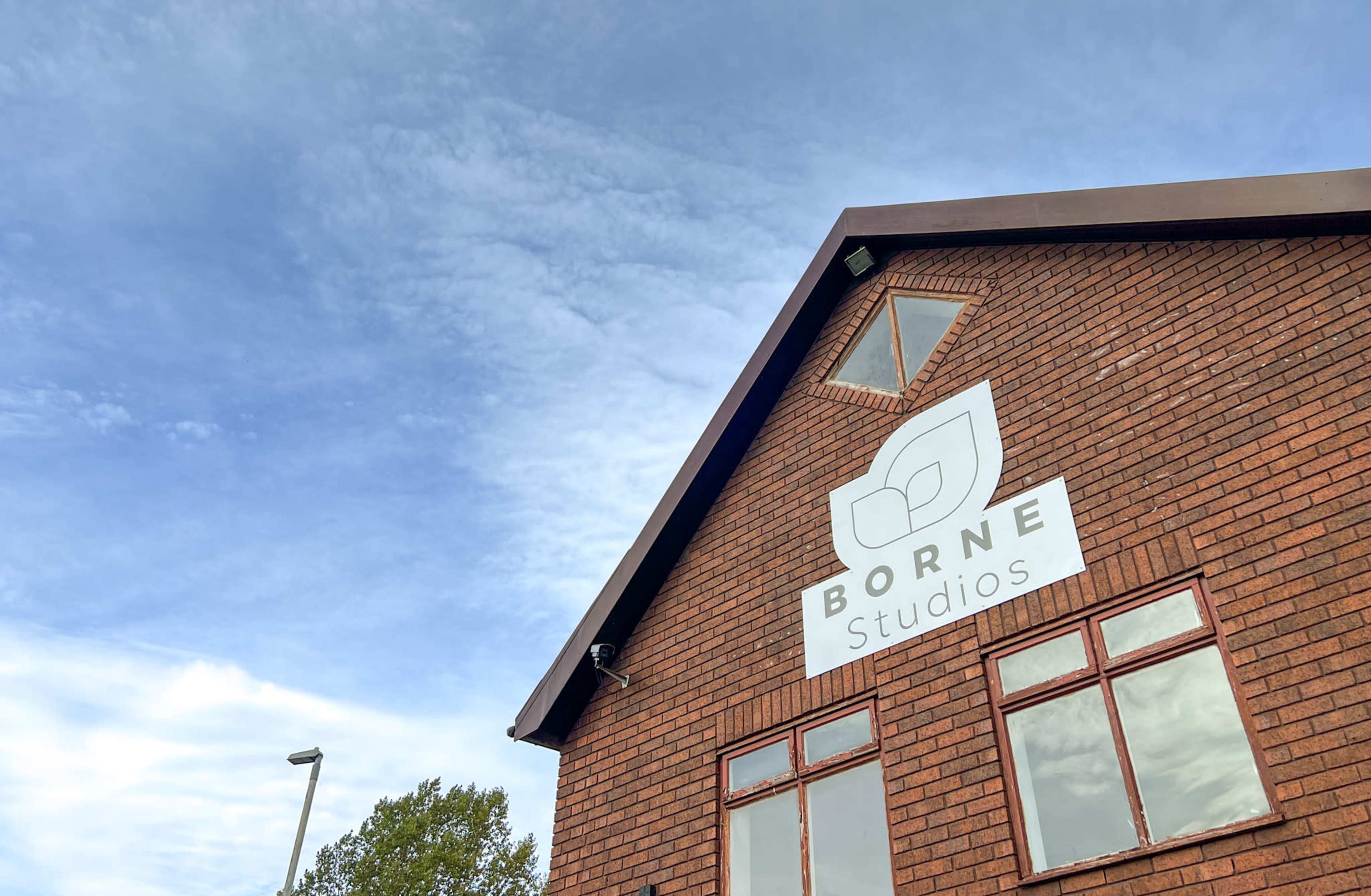 A red brick building with a sign that reads "BORNE Studios" beneath a cloudy blue sky.