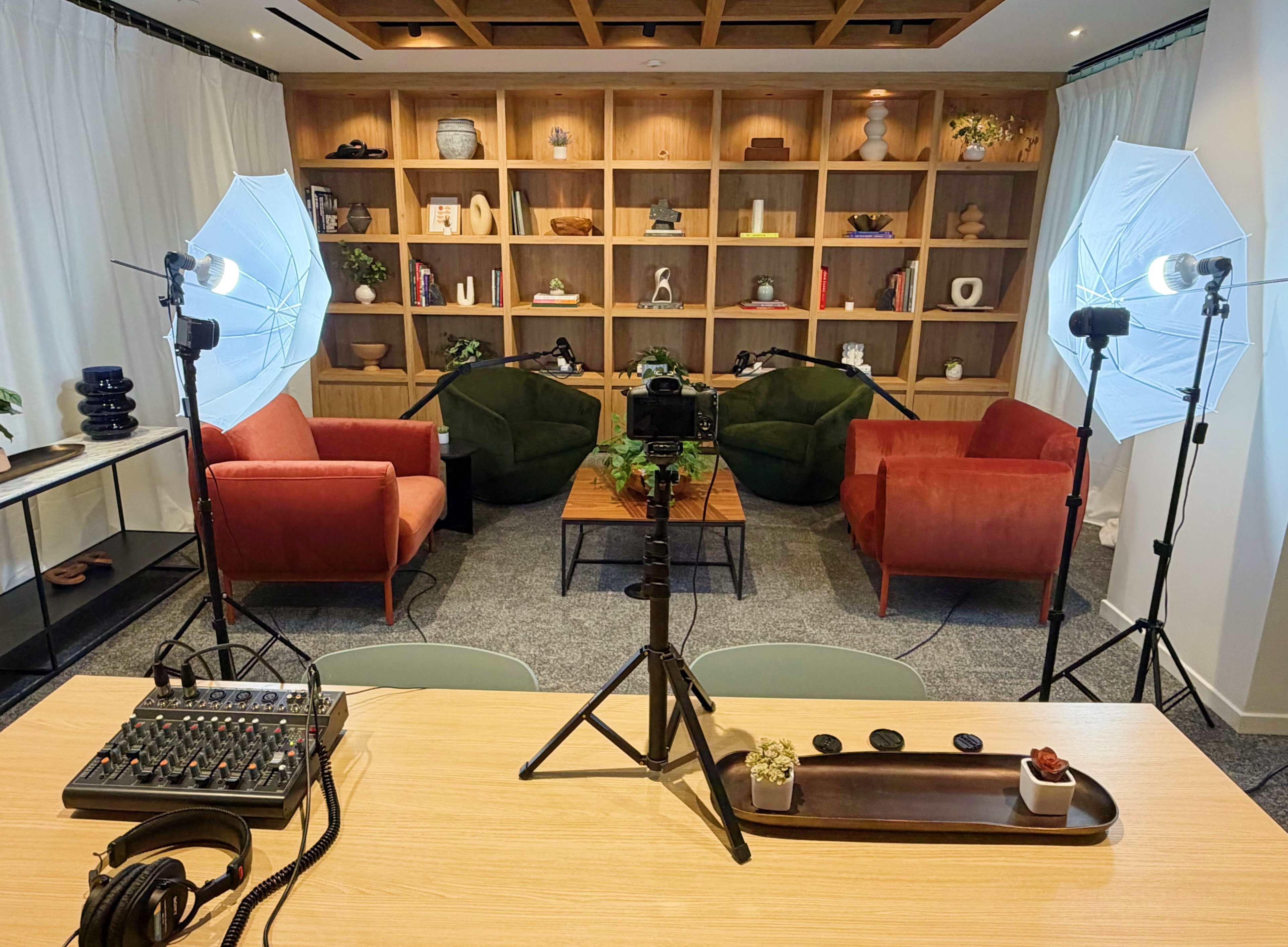The image shows a well-lit modern room featuring two green and two red armchairs, a coffee table, and a wooden shelving unit filled with decorative items.