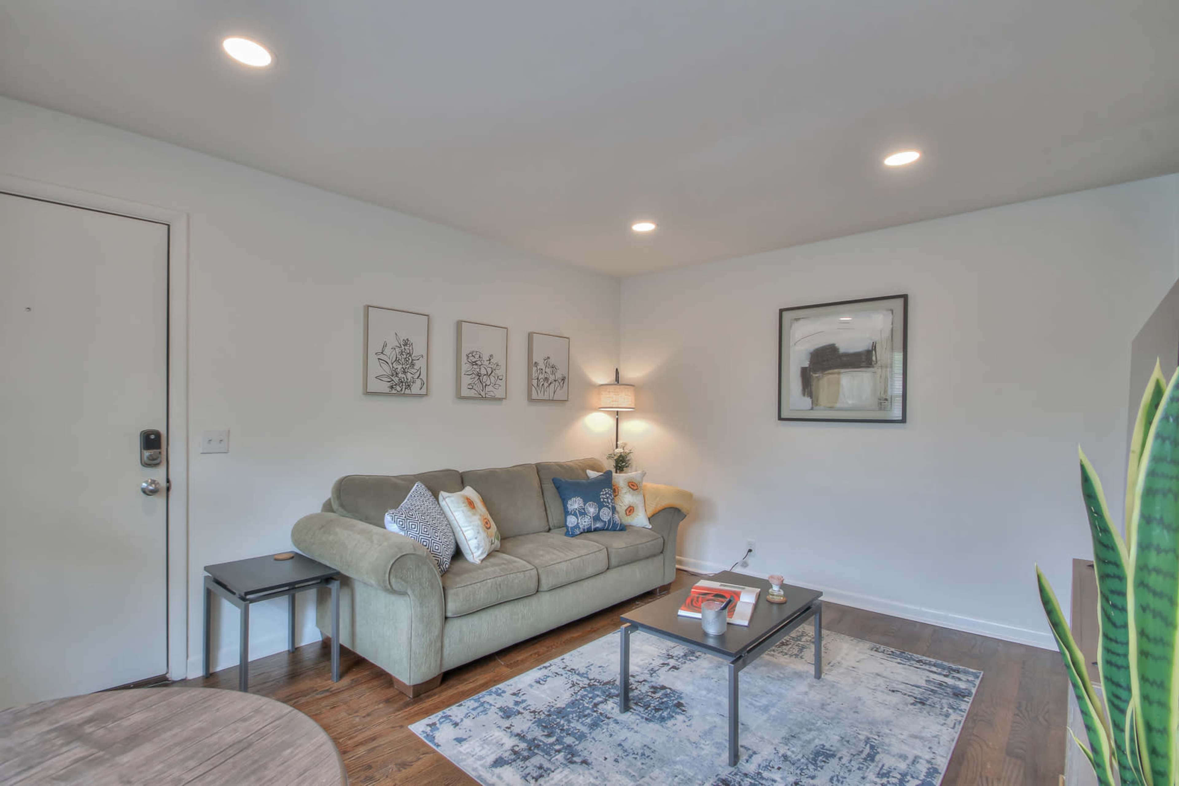 A modern living room features a green sofa, a coffee table, and artwork on the walls, with warm lighting and hardwood floors.