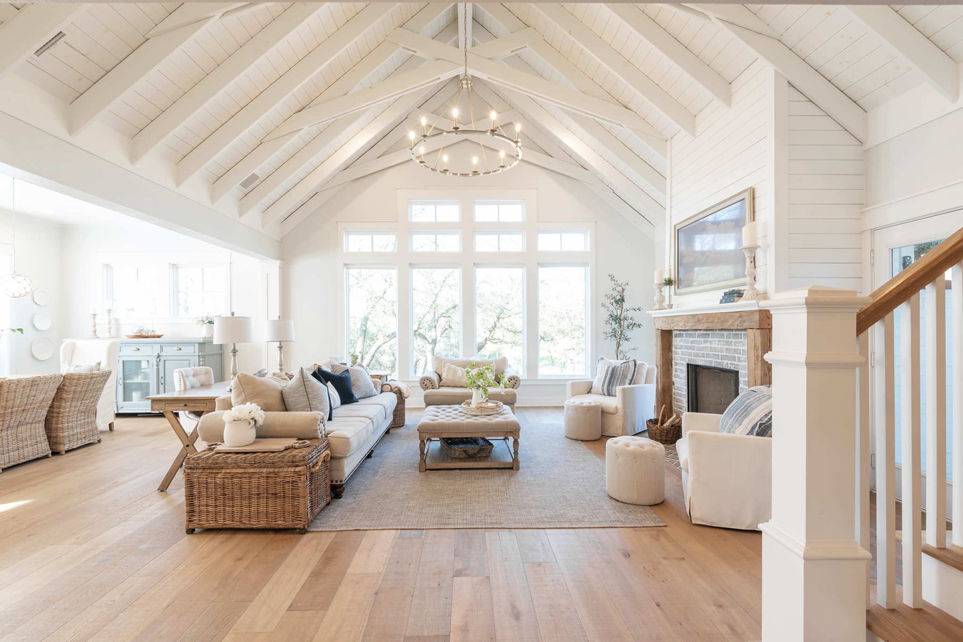 A spacious living room features vaulted ceilings, large windows, a fireplace, and a mix of natural wood and white decor.